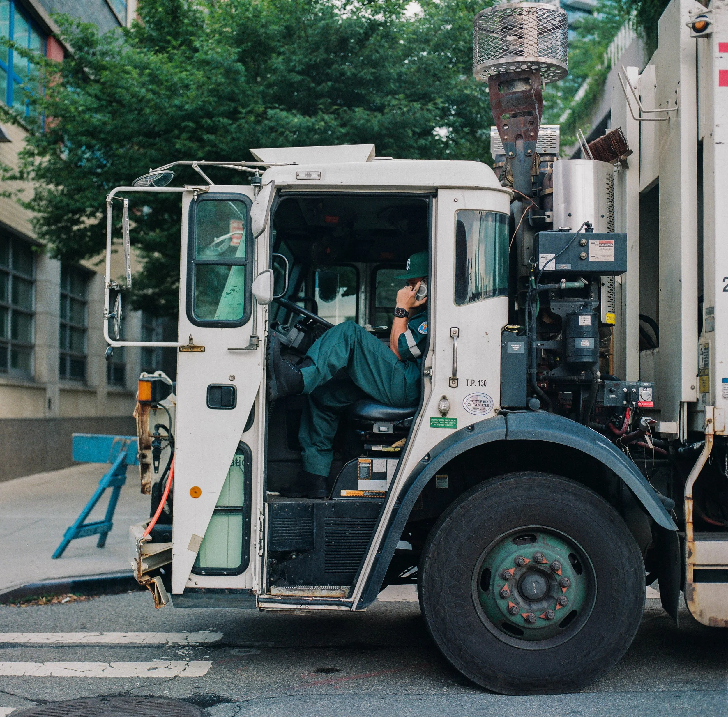 A worker sitting inside a street maintenance vehicle, holding a phone to his ear, parked on a city street.