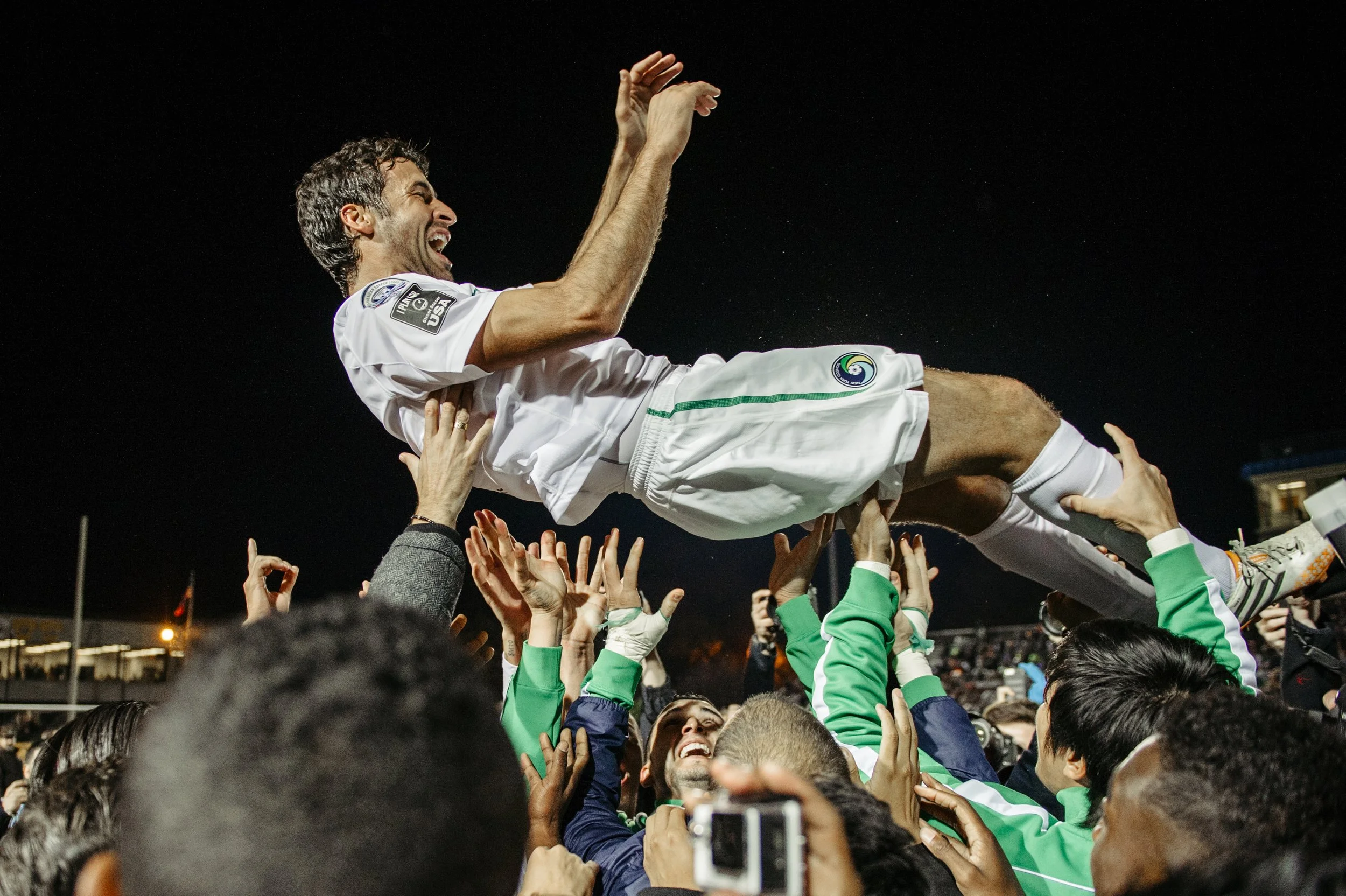 A soccer player being lifted by fans during a celebration at night.