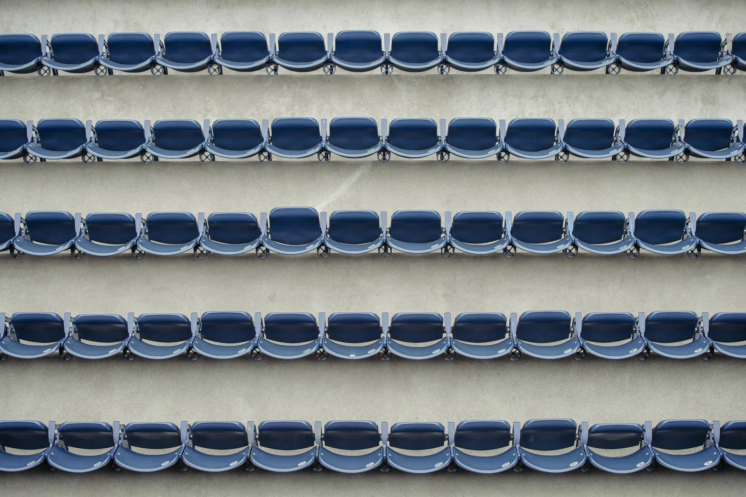Empty blue stadium seats arranged in rows on a concrete surface, viewed from above.