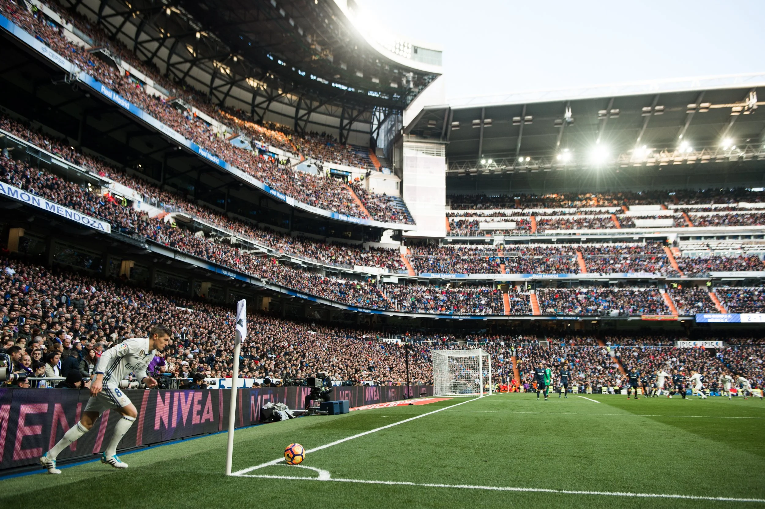 A soccer match in a large stadium filled with spectators, with a player preparing to take a corner kick near the corner flag.
