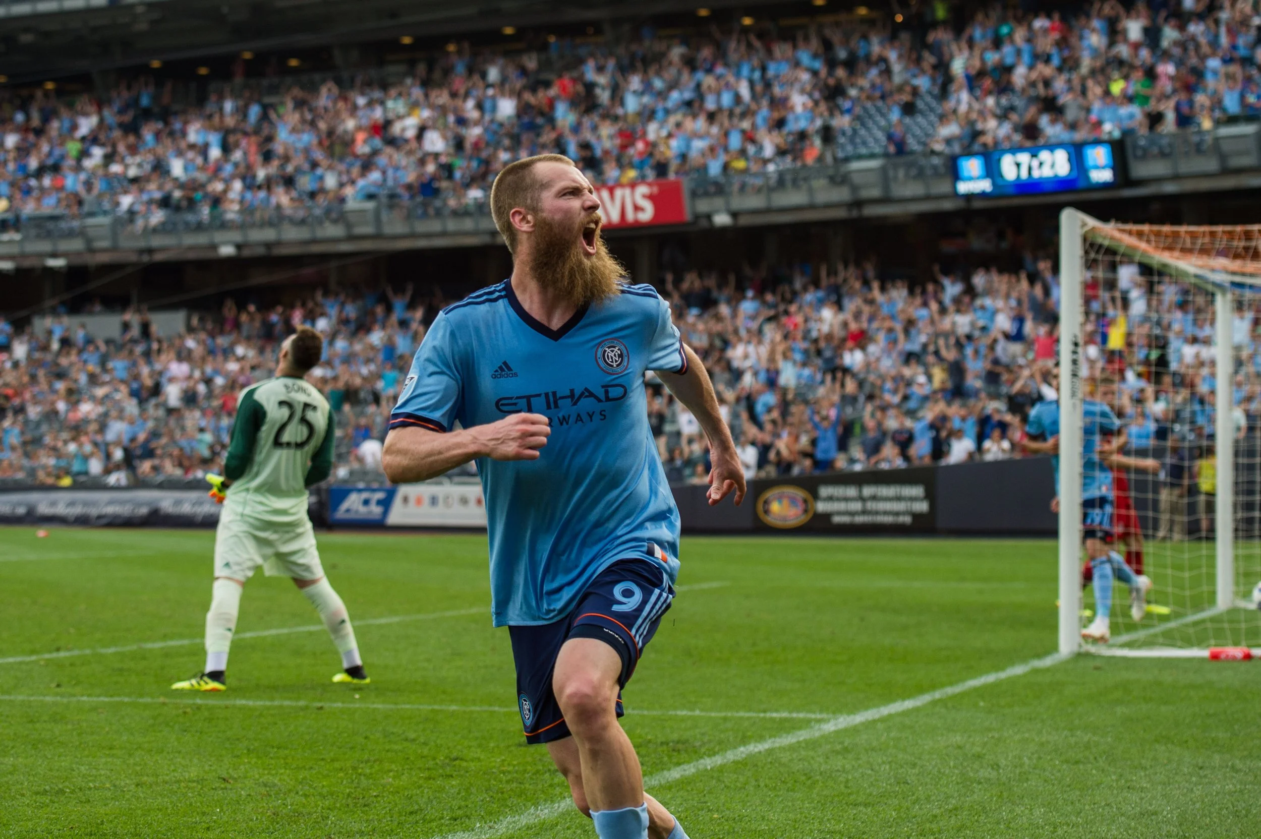 Soccer player in blue uniform celebrating on the field with crowd in the background.