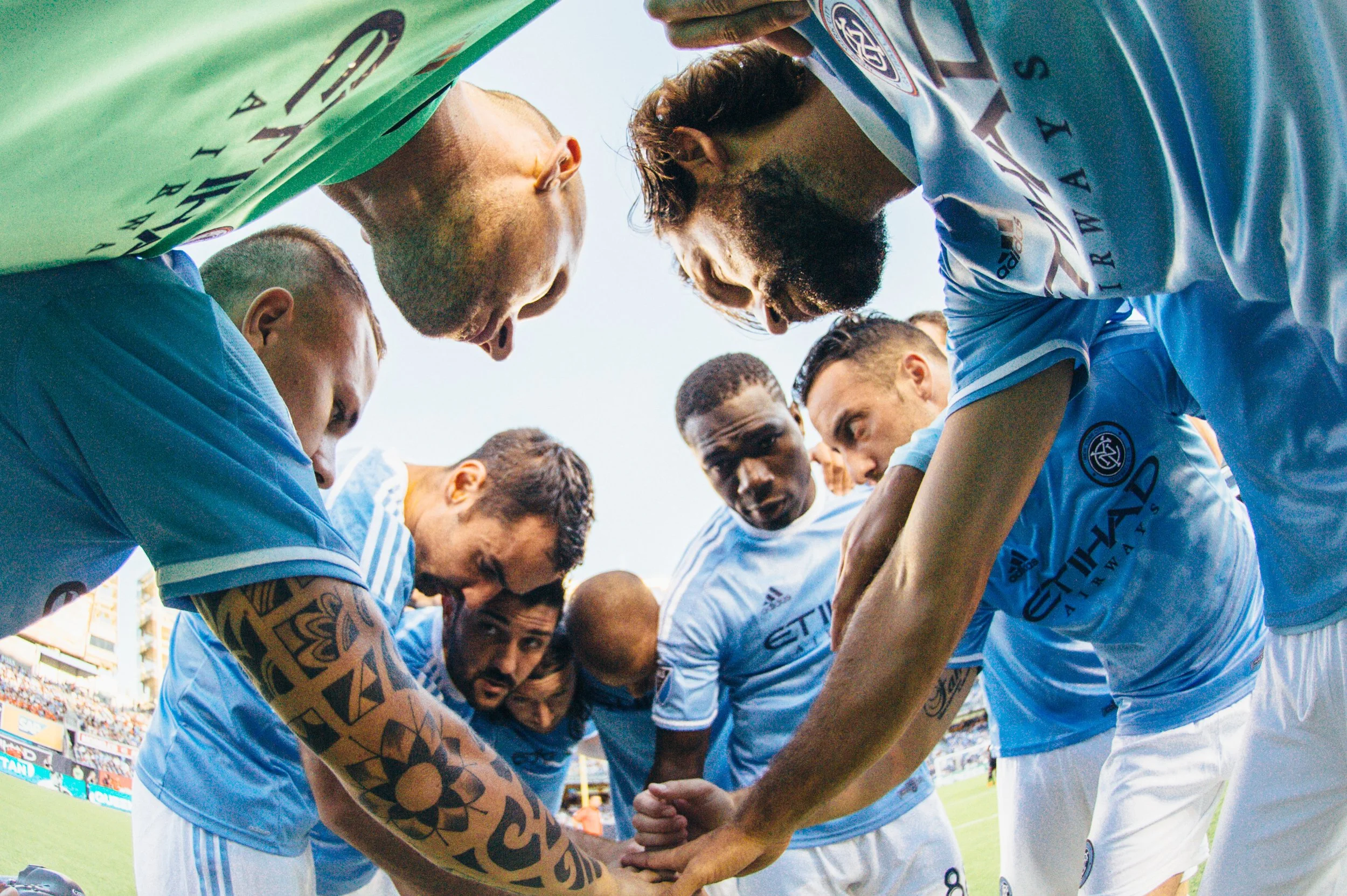 Soccer team in a huddle during a match, players with intense expressions, standing on the field in their blue uniforms.