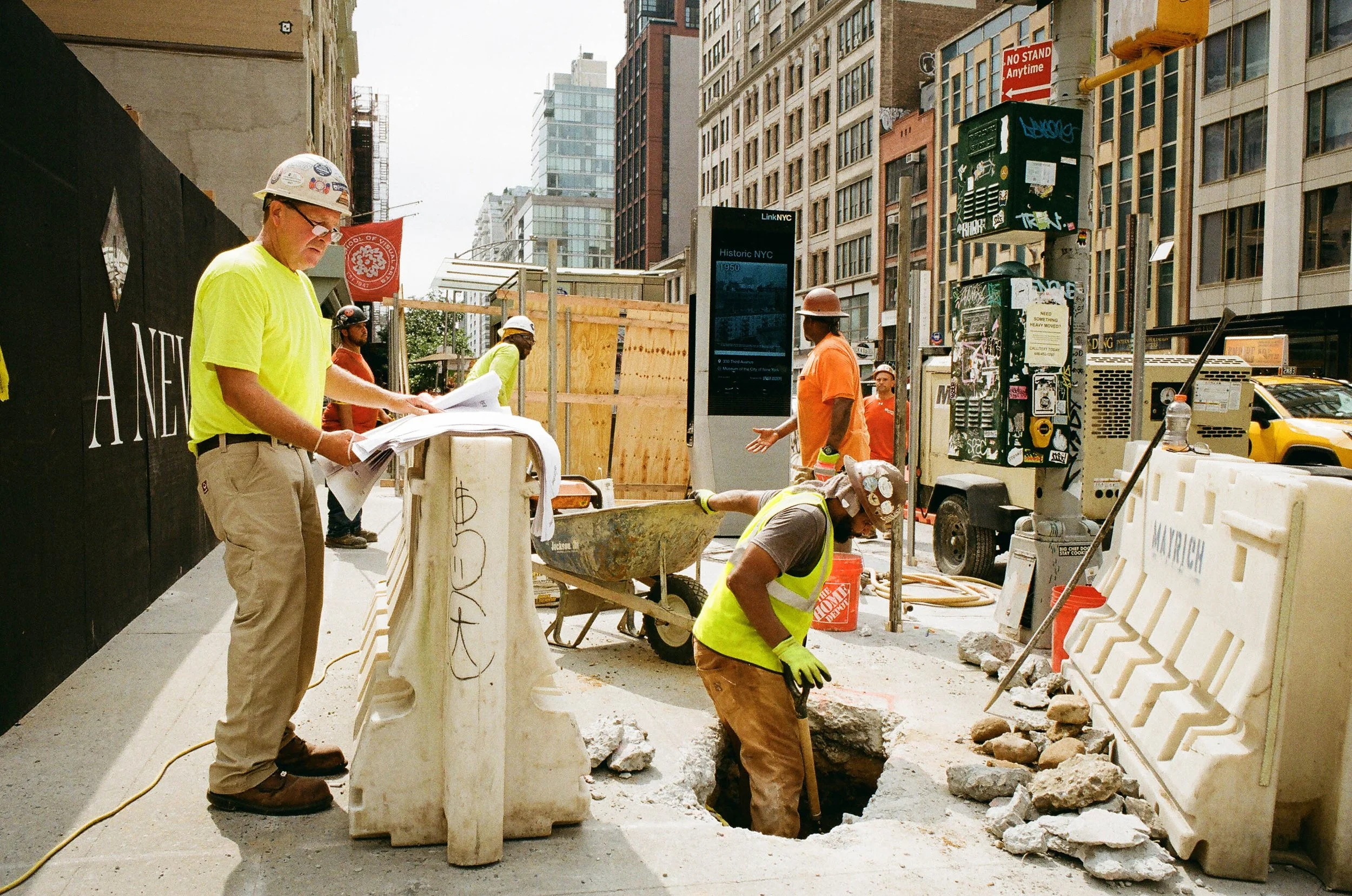Construction workers working on a sidewalk in City NY, with barriers, tools, and equipment around.