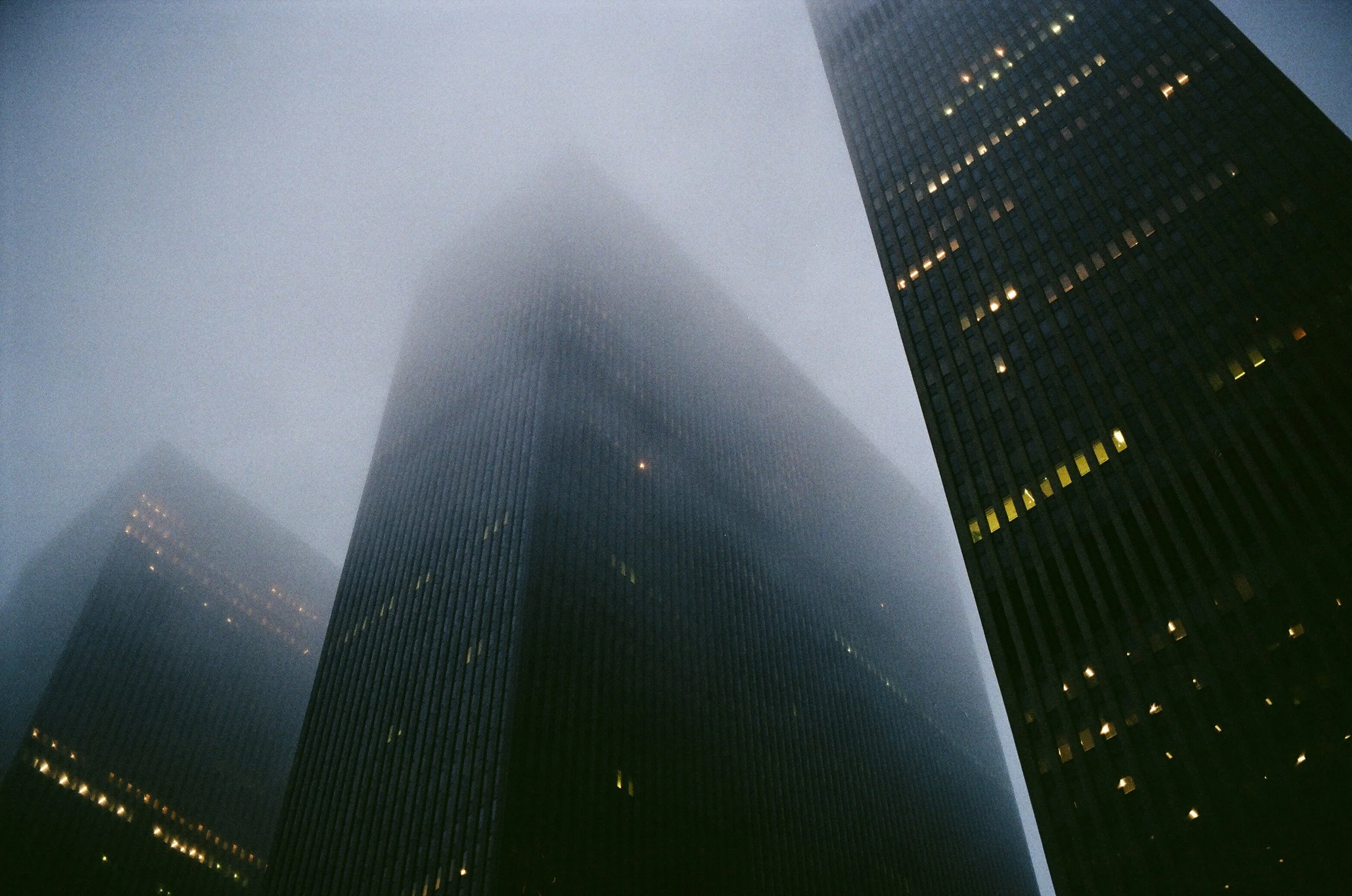 Tall skyscrapers in a foggy city, with some lights on in the buildings.