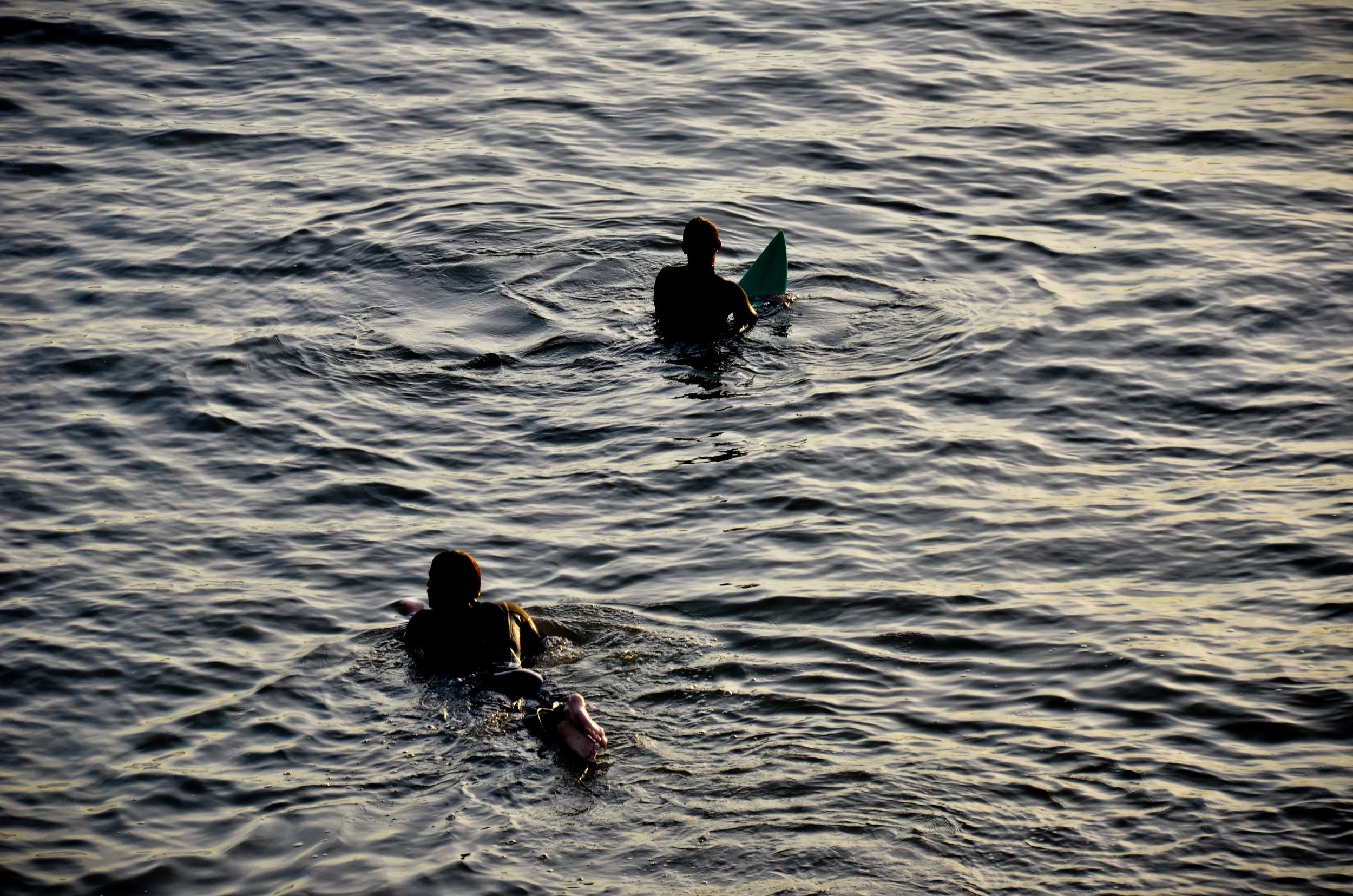 Two people swimming in a body of water, one holding a paddleboard, during sunset or sunrise.