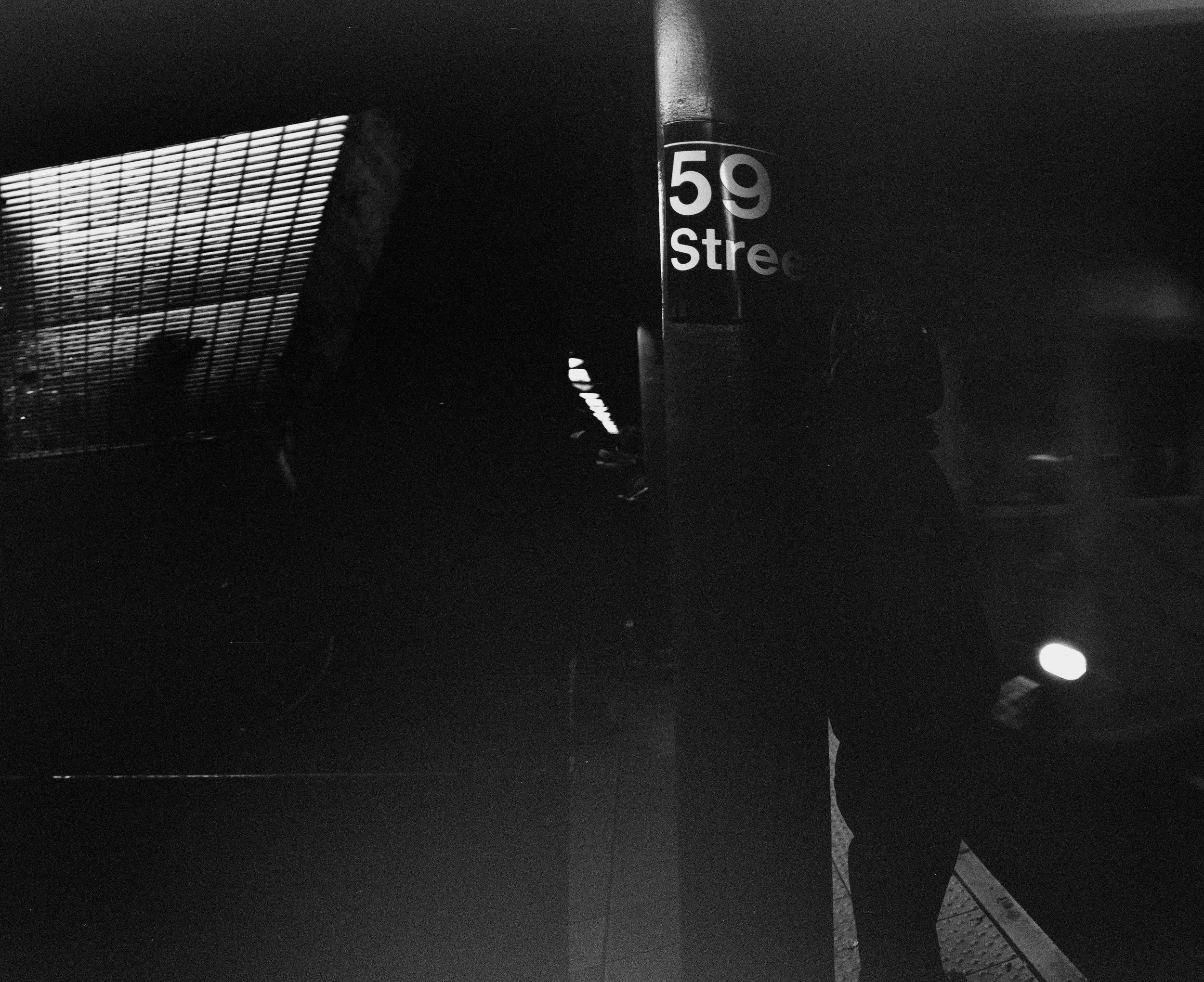 Dark image of people in silhouette, with a sign that reads '59 Street'.