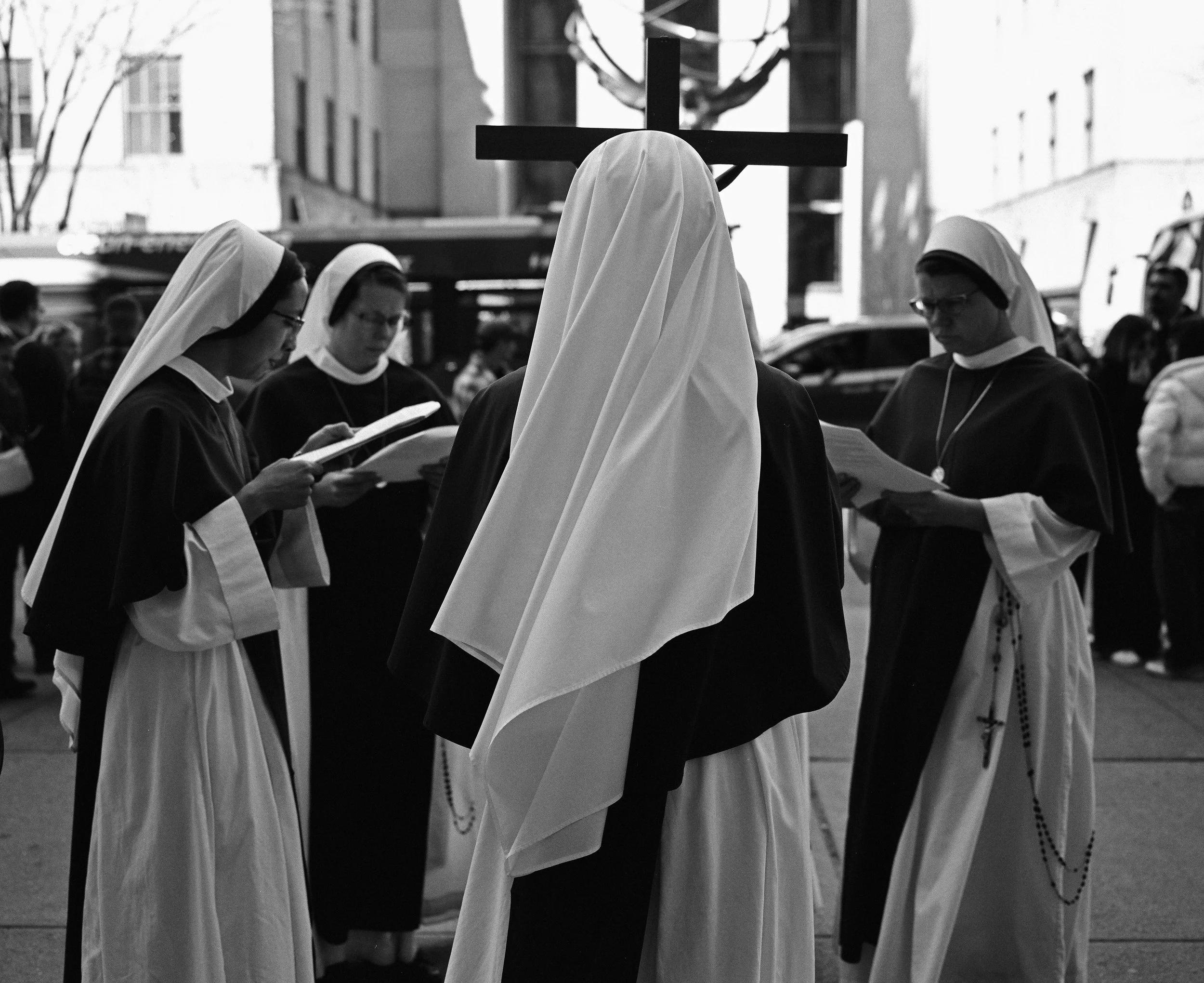 A group of nuns and a person dressed as Jesus Christ praying outdoors around a cross during the daytime.