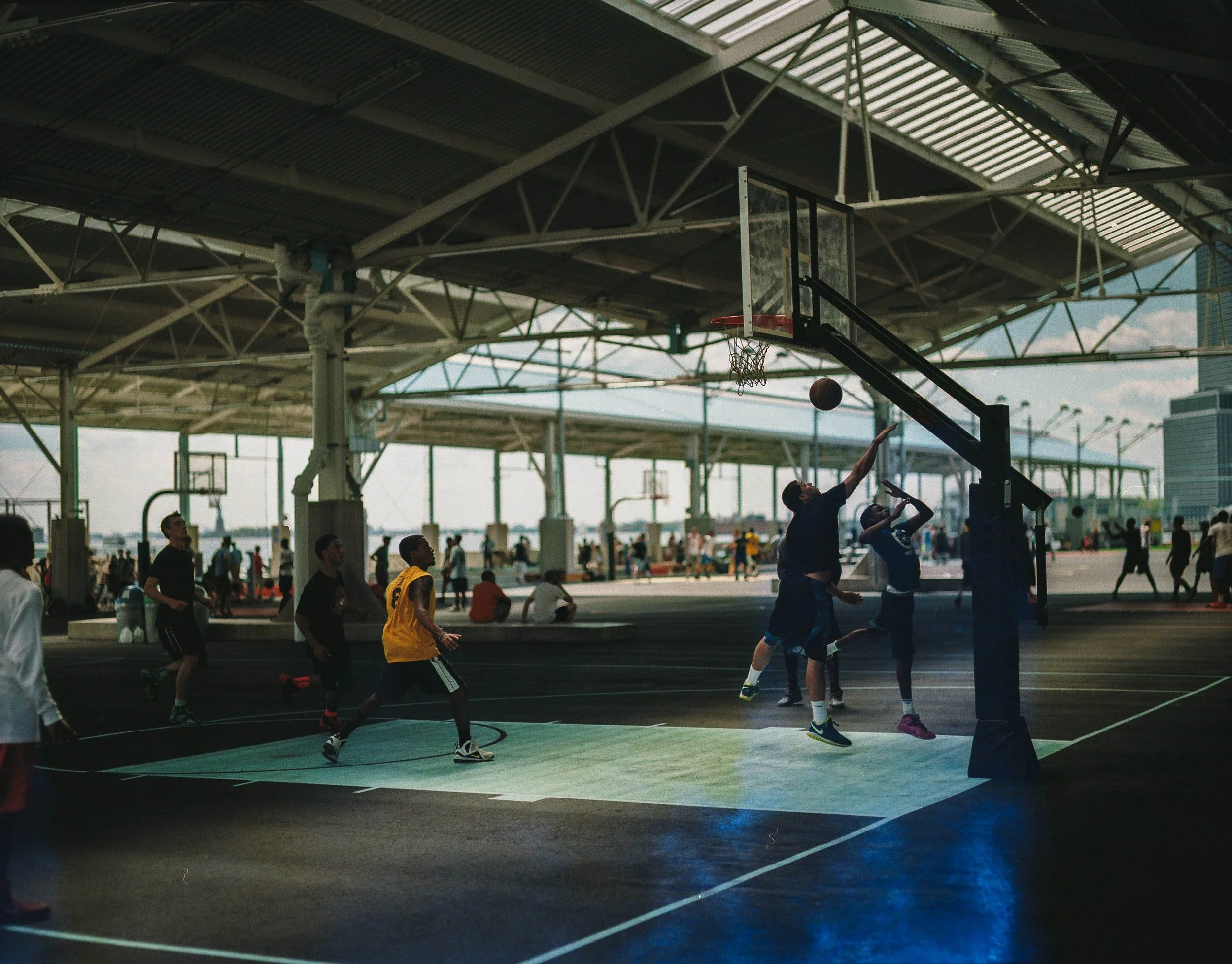 Children playing basketball indoors under a large covered structure.