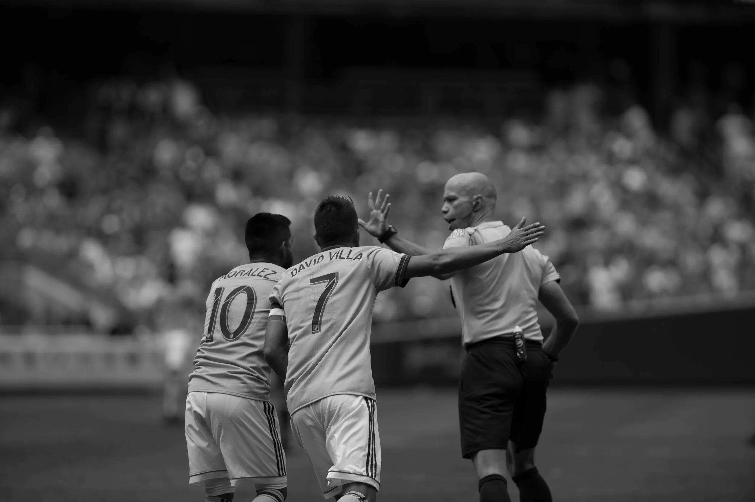 Two soccer players, one with the name 'GRALEZ' and the number 10, and the other with the name 'DAVID VILLA' and the number 7, are celebrating with a referee on the soccer field.