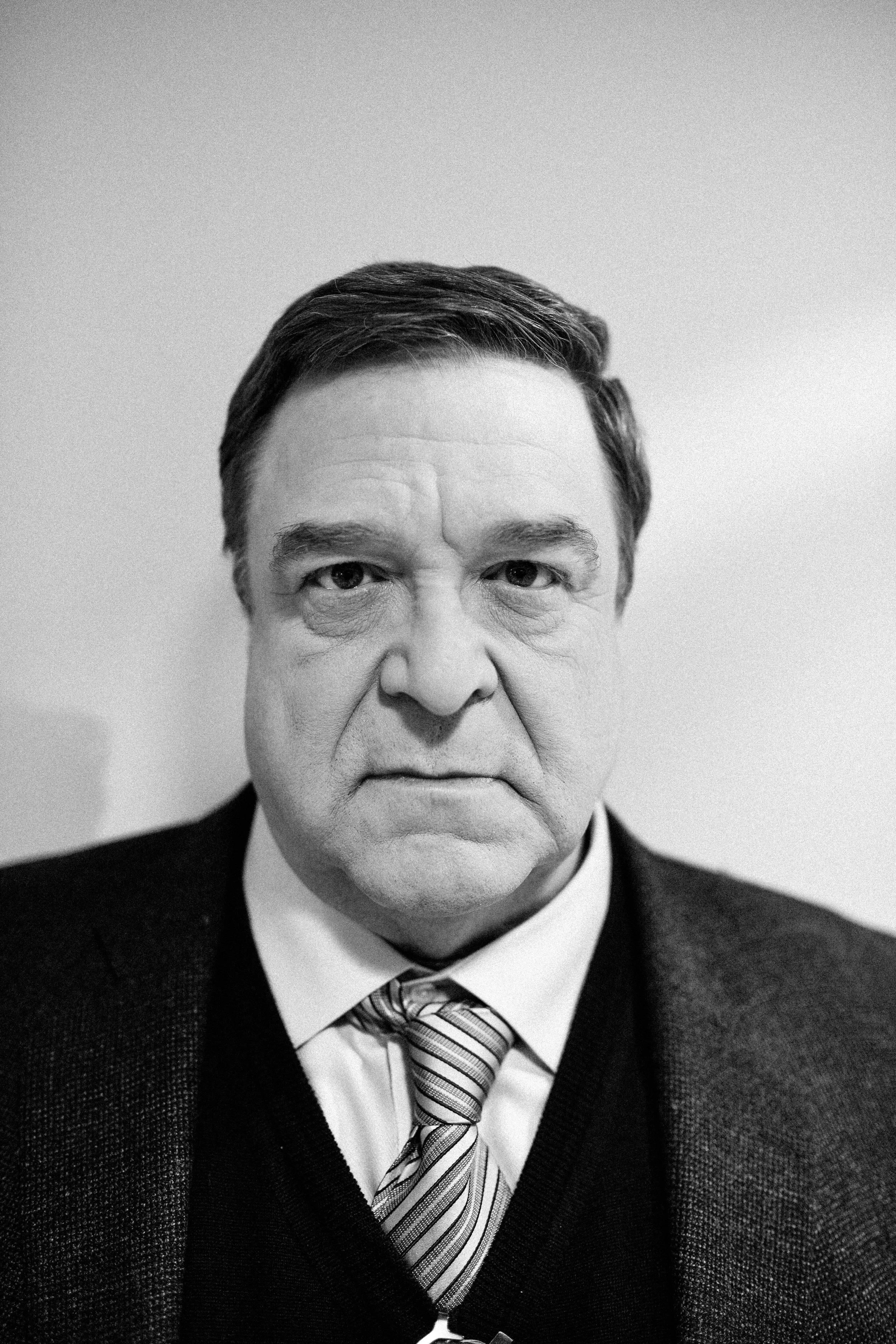 Black and white portrait of an older man with a stern expression, wearing a suit, dress shirt, tie, and blazer, against a plain background.