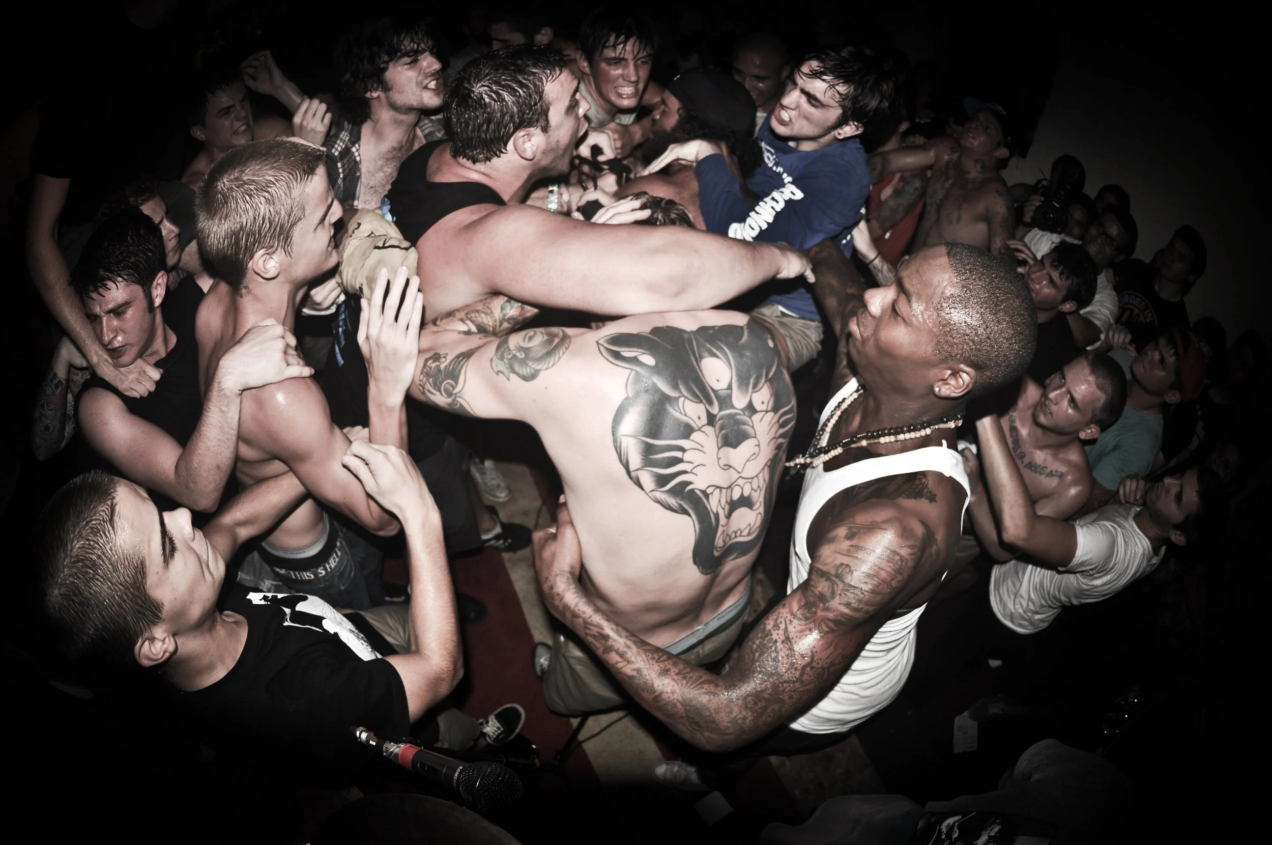 People fighting in a crowded room, with some grabbing or pushing each other aggressively.