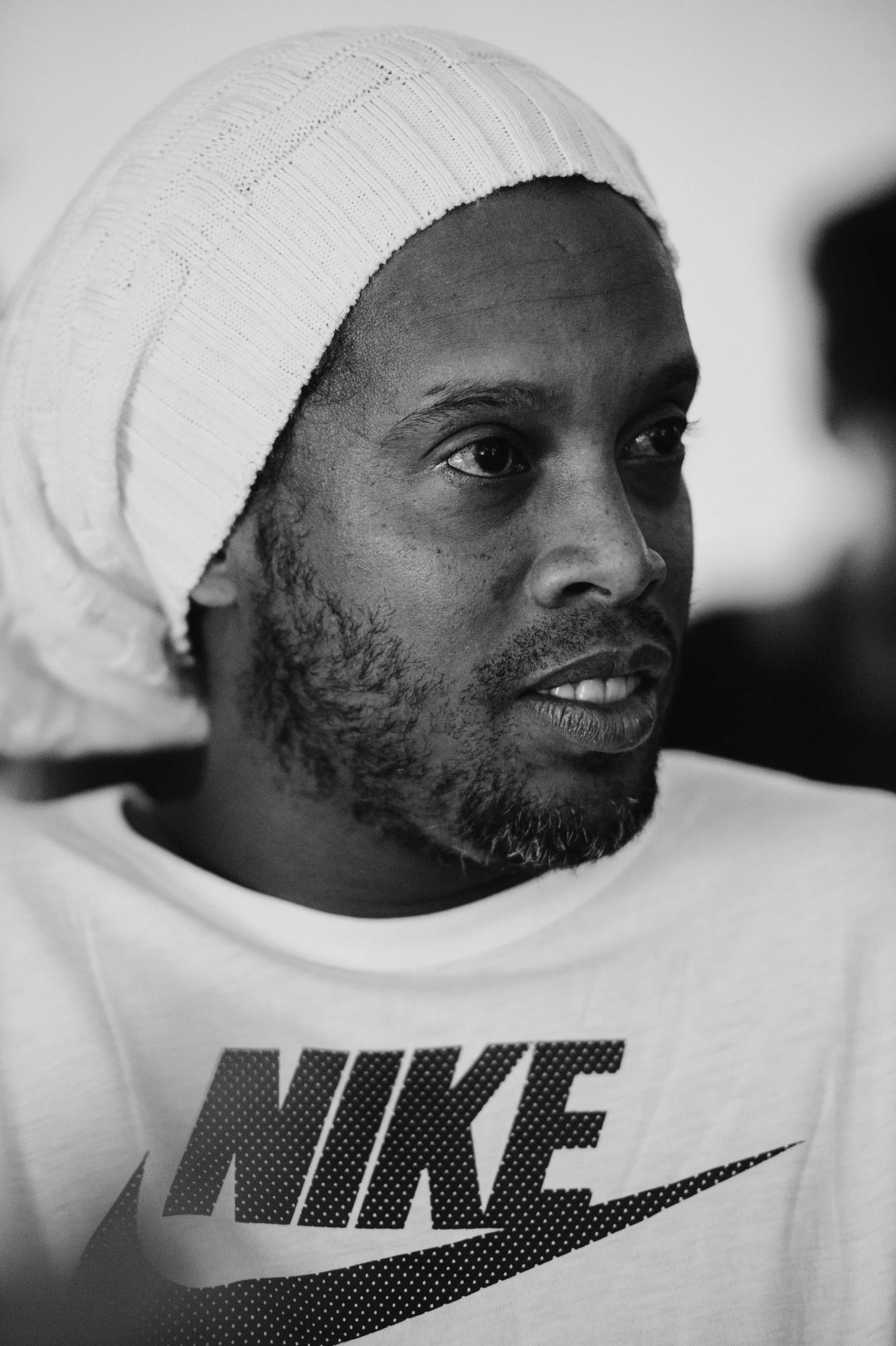 A black and white close-up of a man wearing a knit hat and a Nike t-shirt, looking to the side.