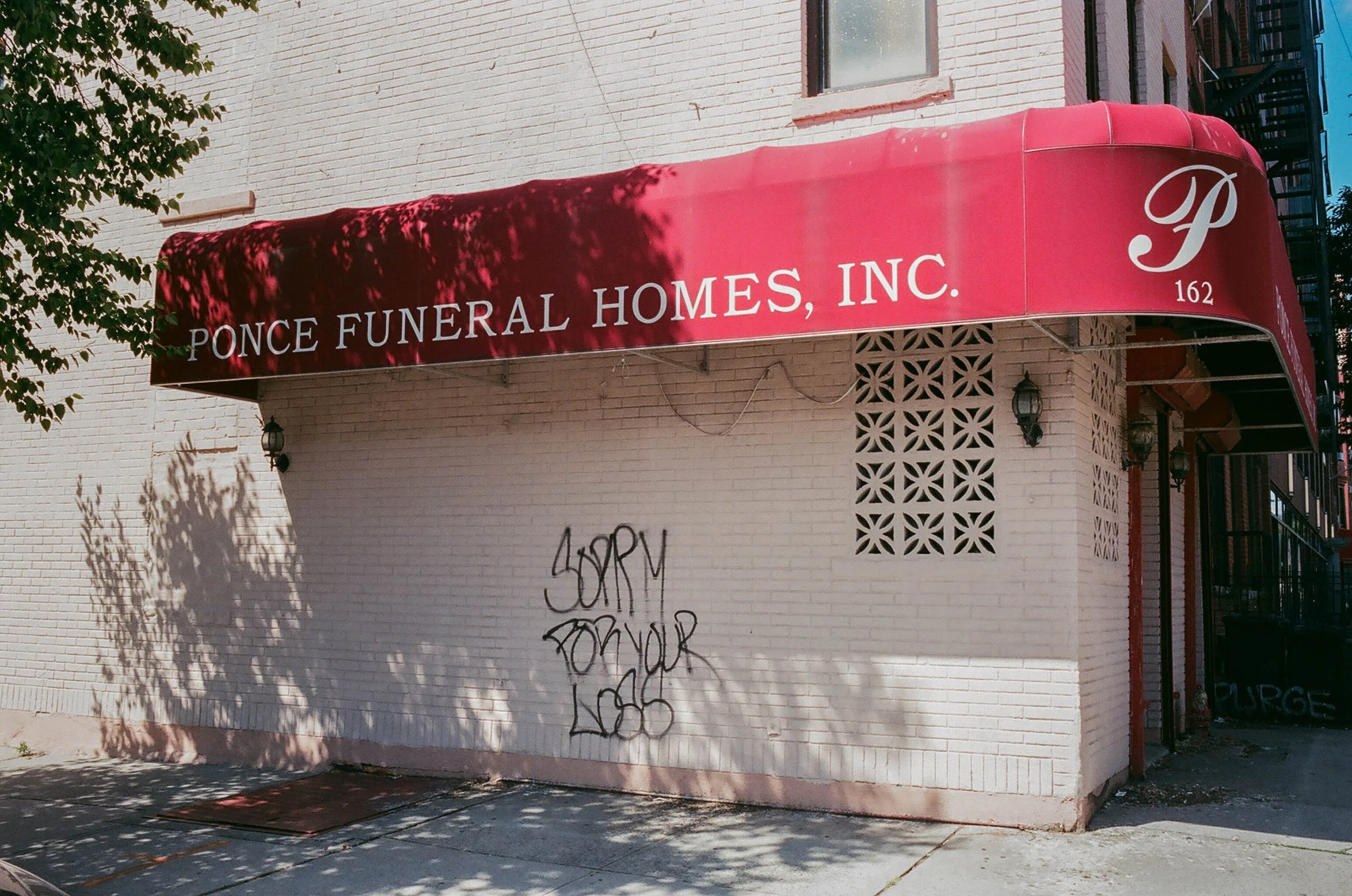 Building with a red awning that reads "Ponce Funeral Homes, Inc." and a white letter P logo, with graffiti on the wall underneath.