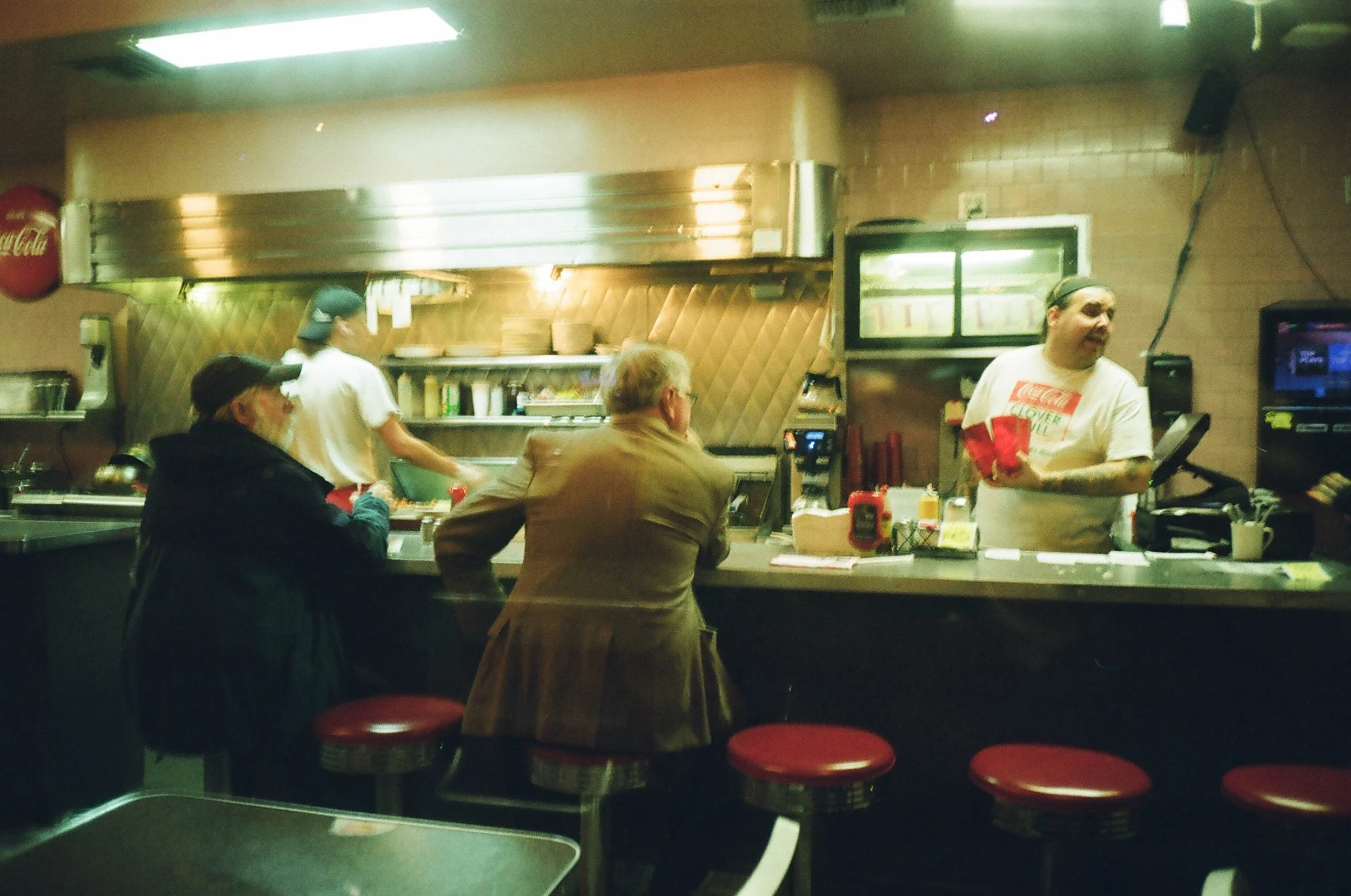 People sitting at a counter in a diner, with a man behind the counter preparing food.