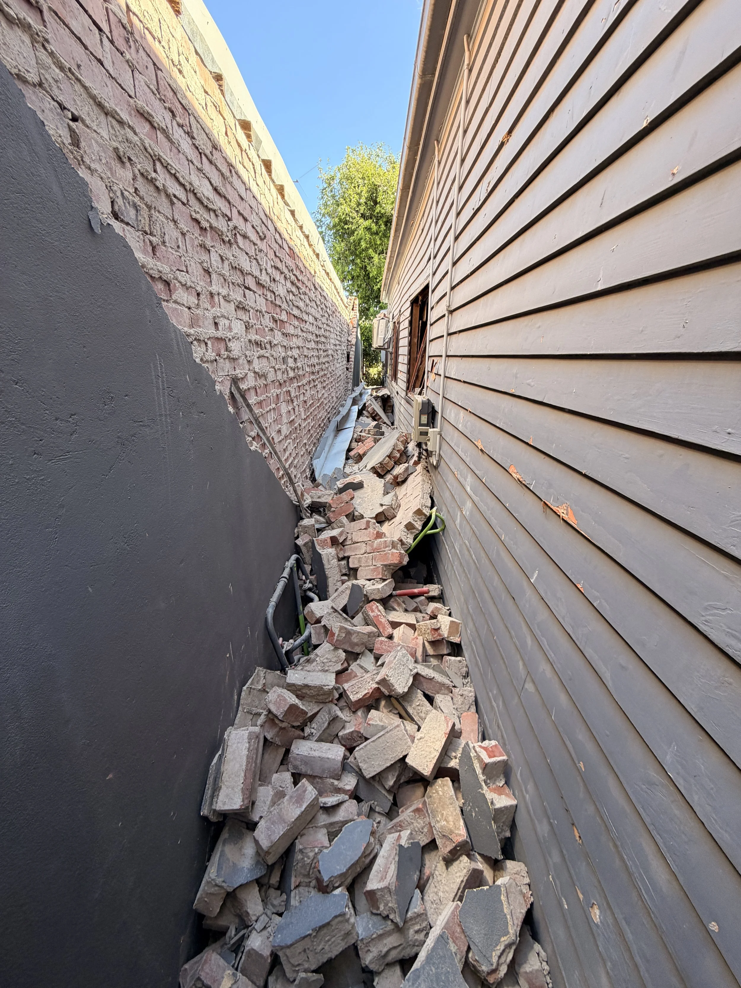 Side of a house with debris and broken bricks on the ground, indicating construction or renovation work.