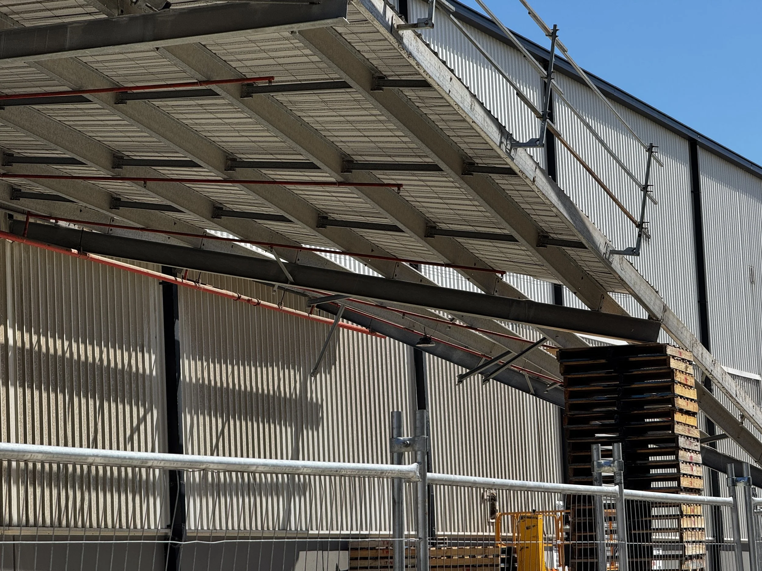 Construction site with scaffolding and steel stairs outside a building with corrugated metal siding.
