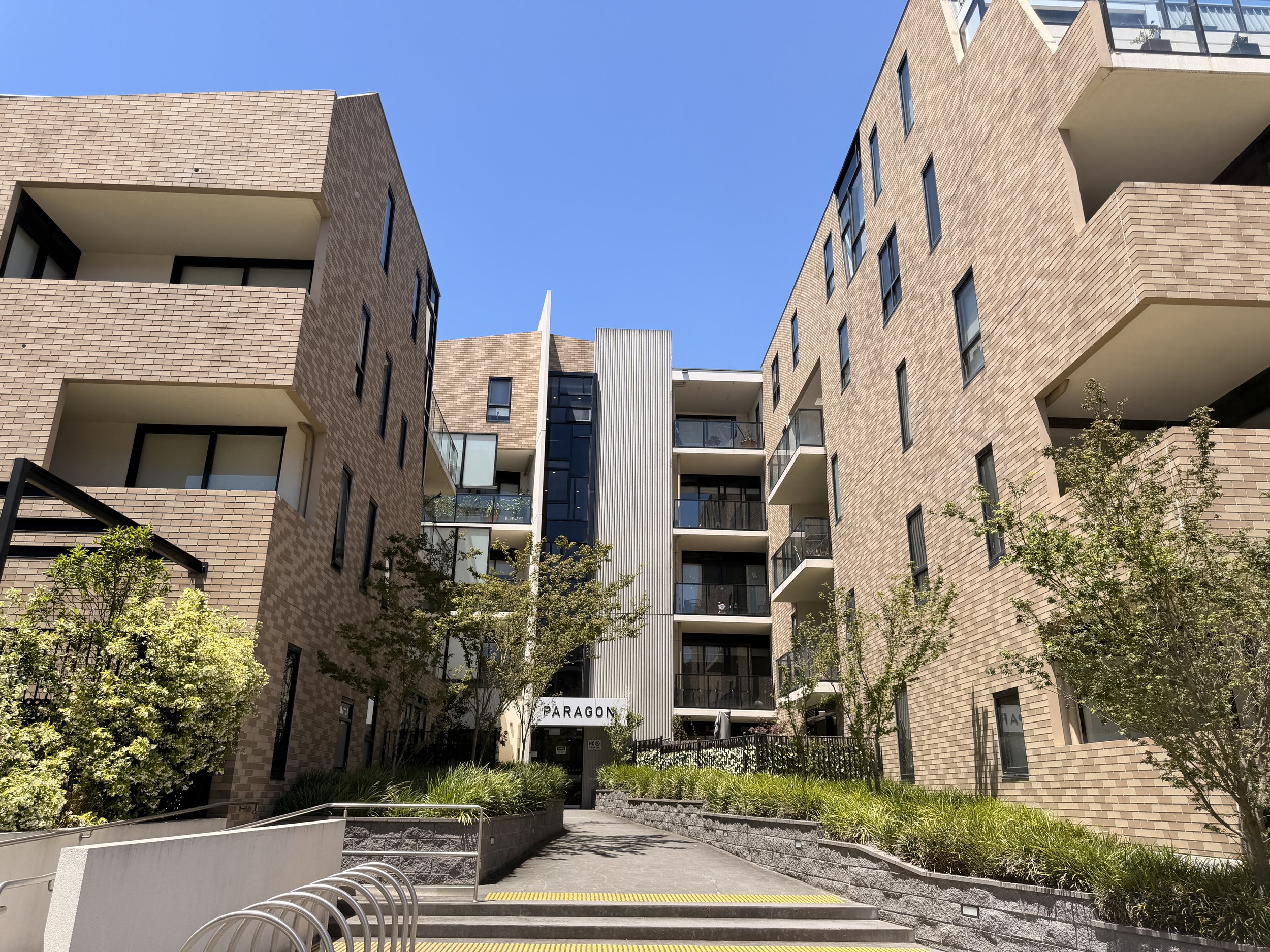 View of modern apartment complex with brick walls, black window frames, and balconies, under a clear blue sky.