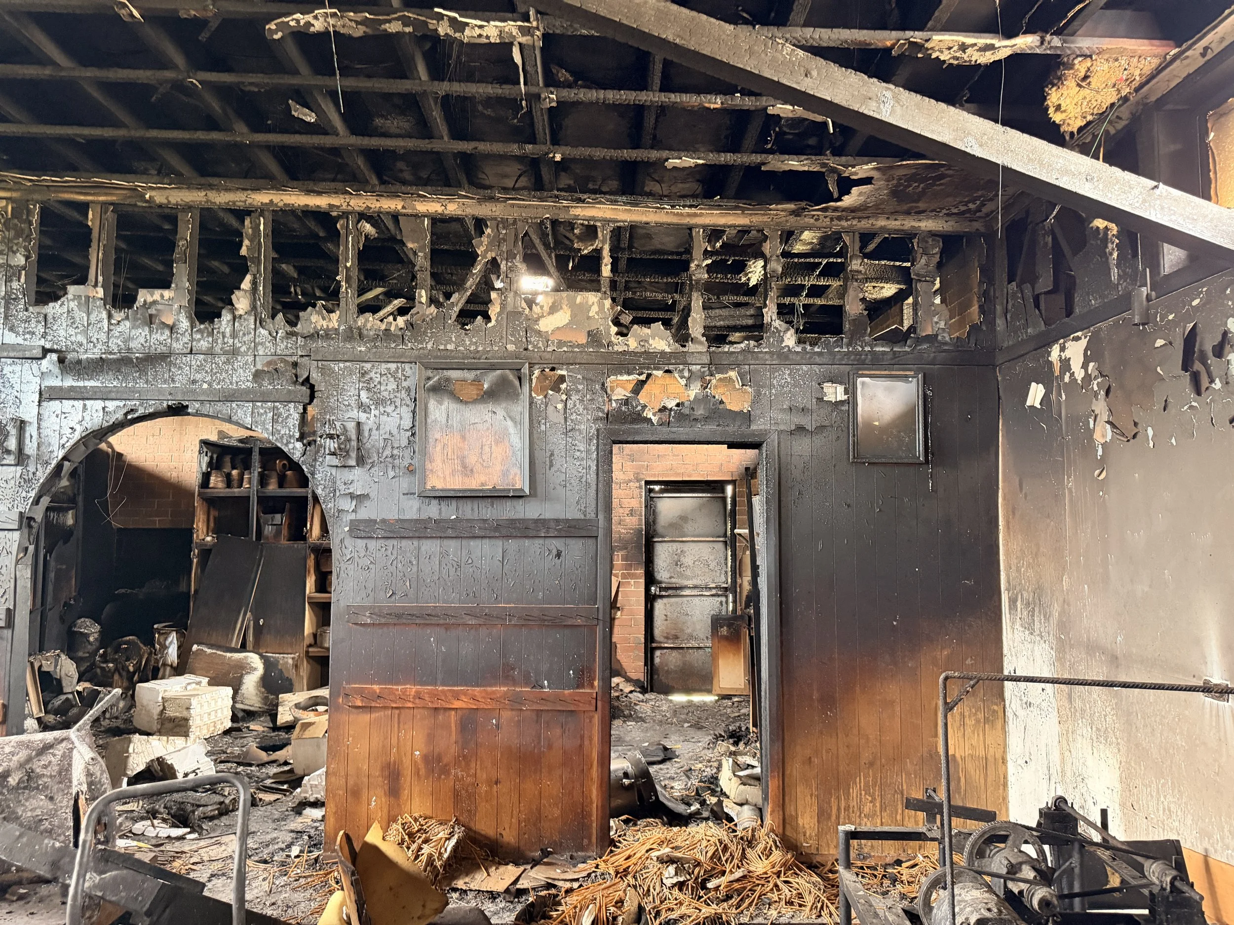 Inside a burned building with charred black walls and ceiling, damaged furniture, debris, and burnt materials.