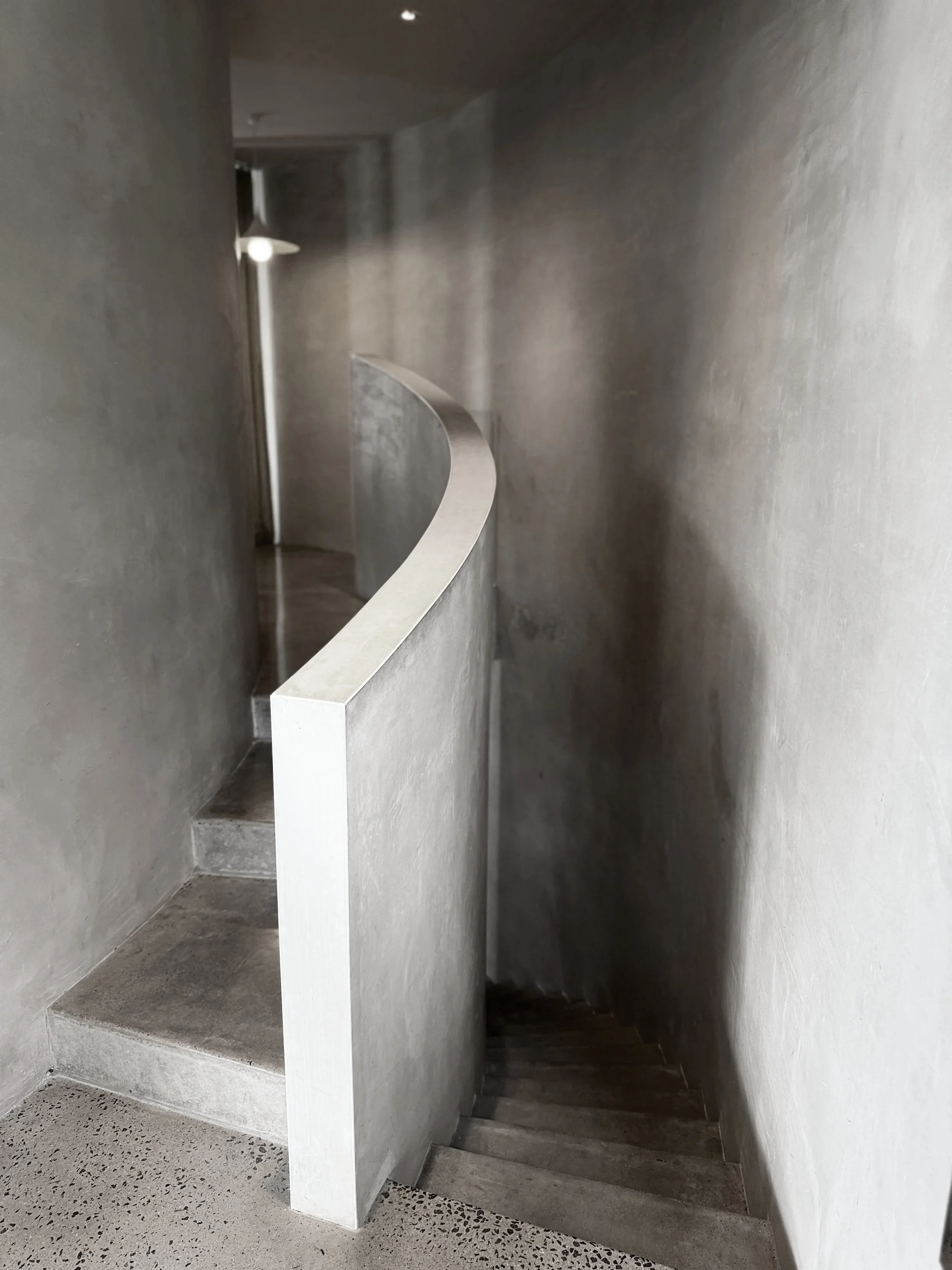 A staircase with a curved concrete wall railing in a dimly lit, modern interior space with concrete walls.