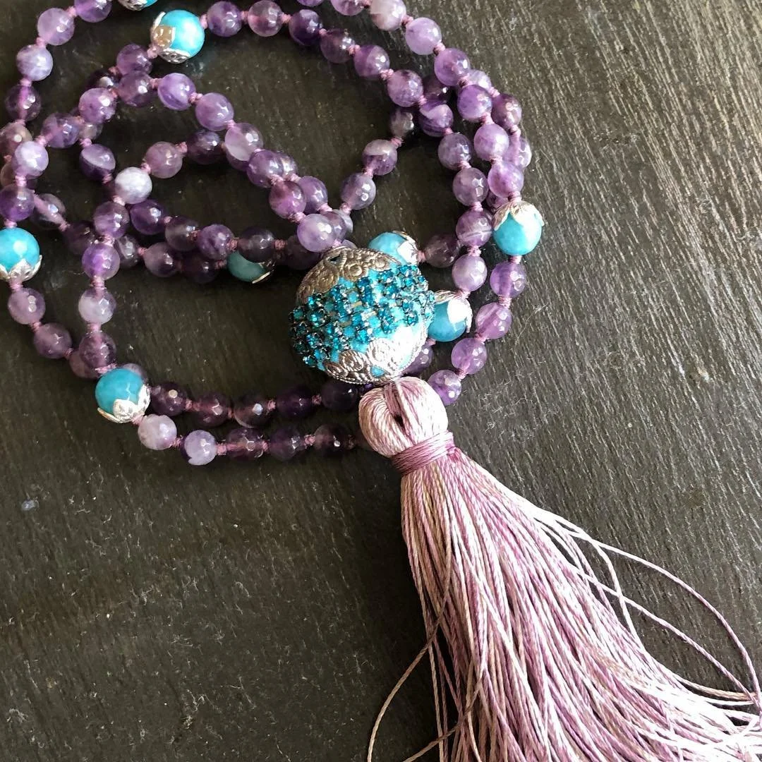 A beaded jewelry piece with purple and turquoise beads, a decorative sphere encrusted with blue rhinestones, and a pink tassel.