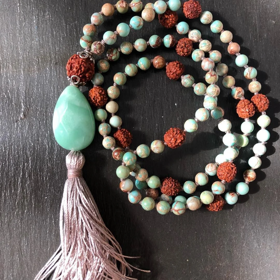 A beaded necklace with turquoise, reddish-brown, and white beads, featuring a large turquoise pendant and a pinkish-gray tassel, laid on a black surface.