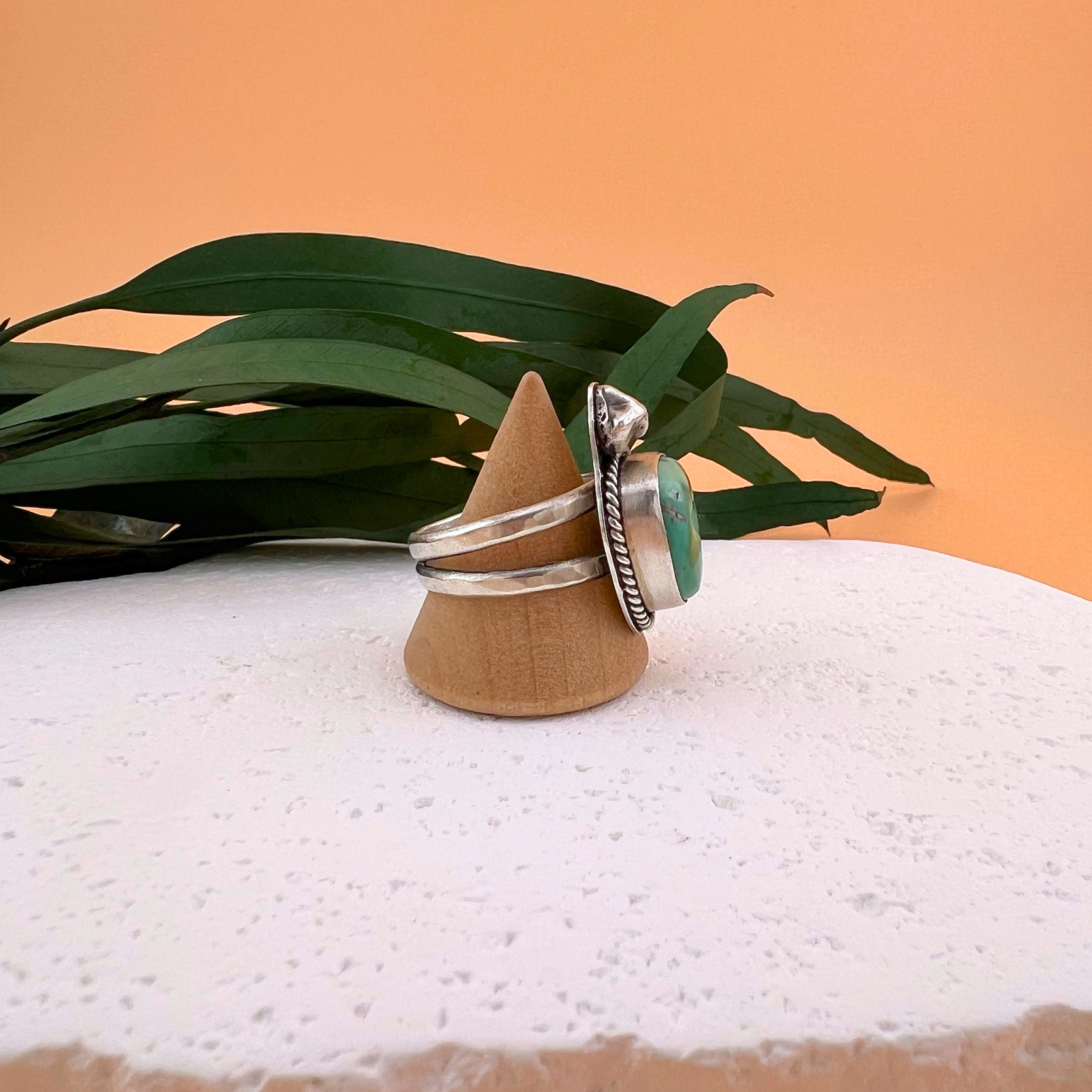 Side view of a one of a kind Royston turquoise nugget ring set in sterling silver with sculptural hand-formed silver accents, displayed on a white stone surface.