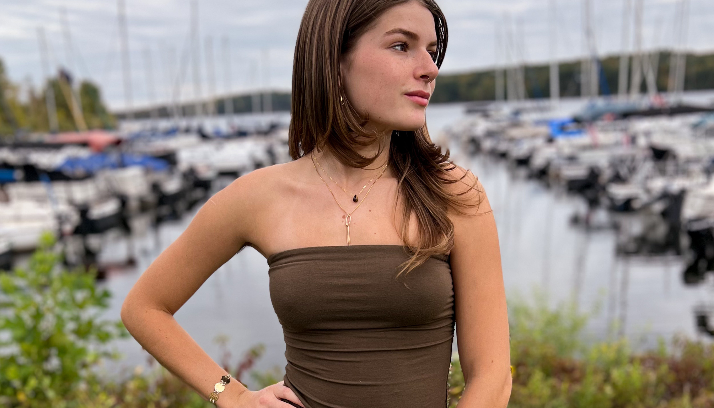 Young woman at a marina looking in the distance, wearing the on the fringe and a tiger's eye necklace.