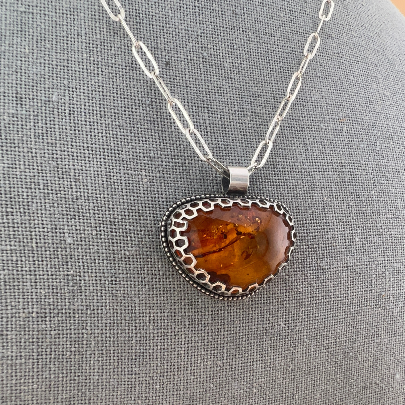 Close-up of honey-toned Baltic amber set in a geometric honeycomb bezel with sterling silver chain.