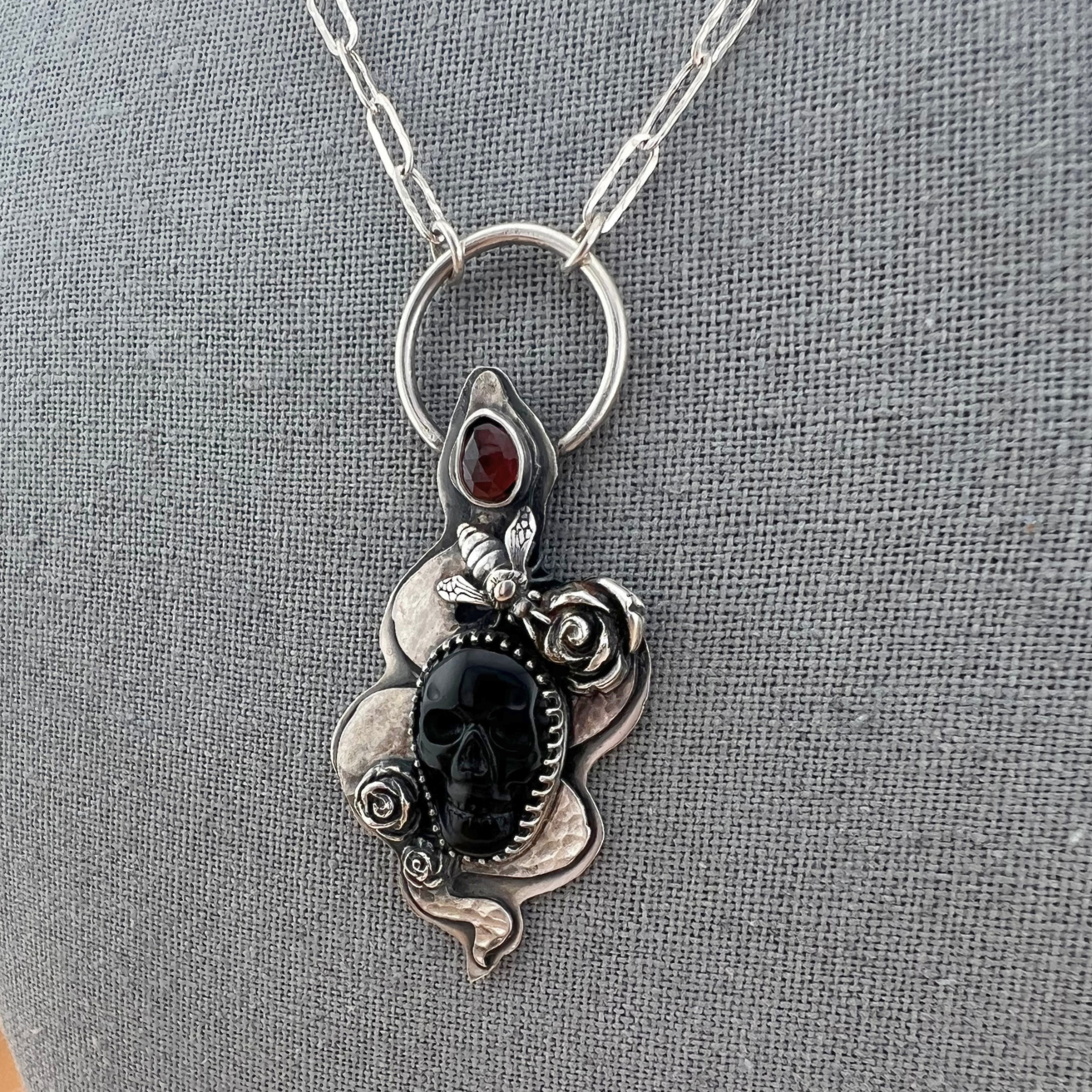 Close up of the sterling silver serpent necklace featuring a hand-carved onyx skull with faceted garnet accents.