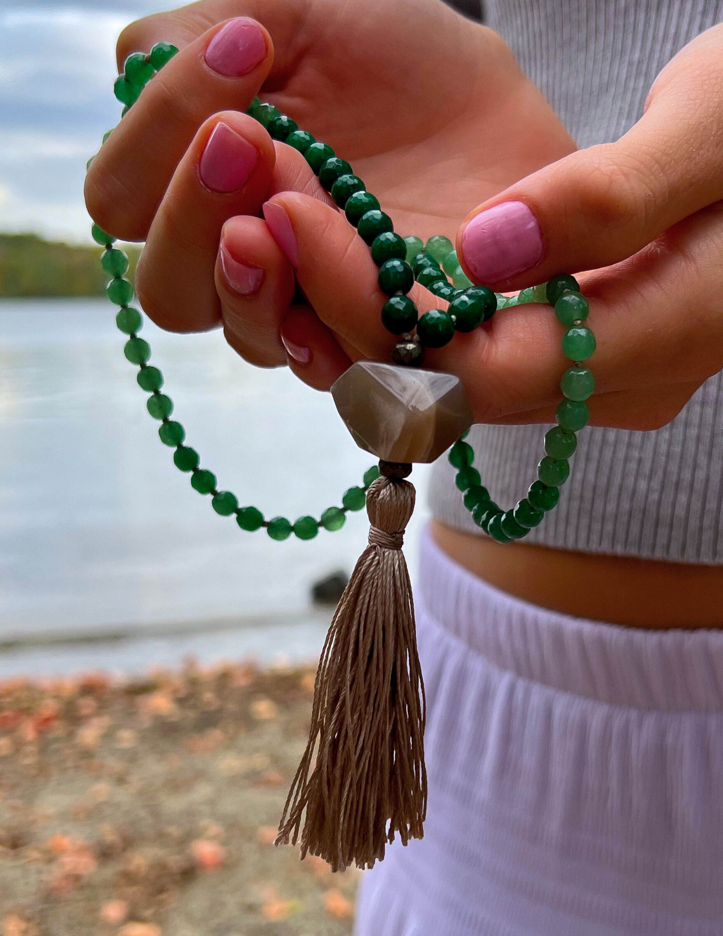 two hands holding a green jade mala.
