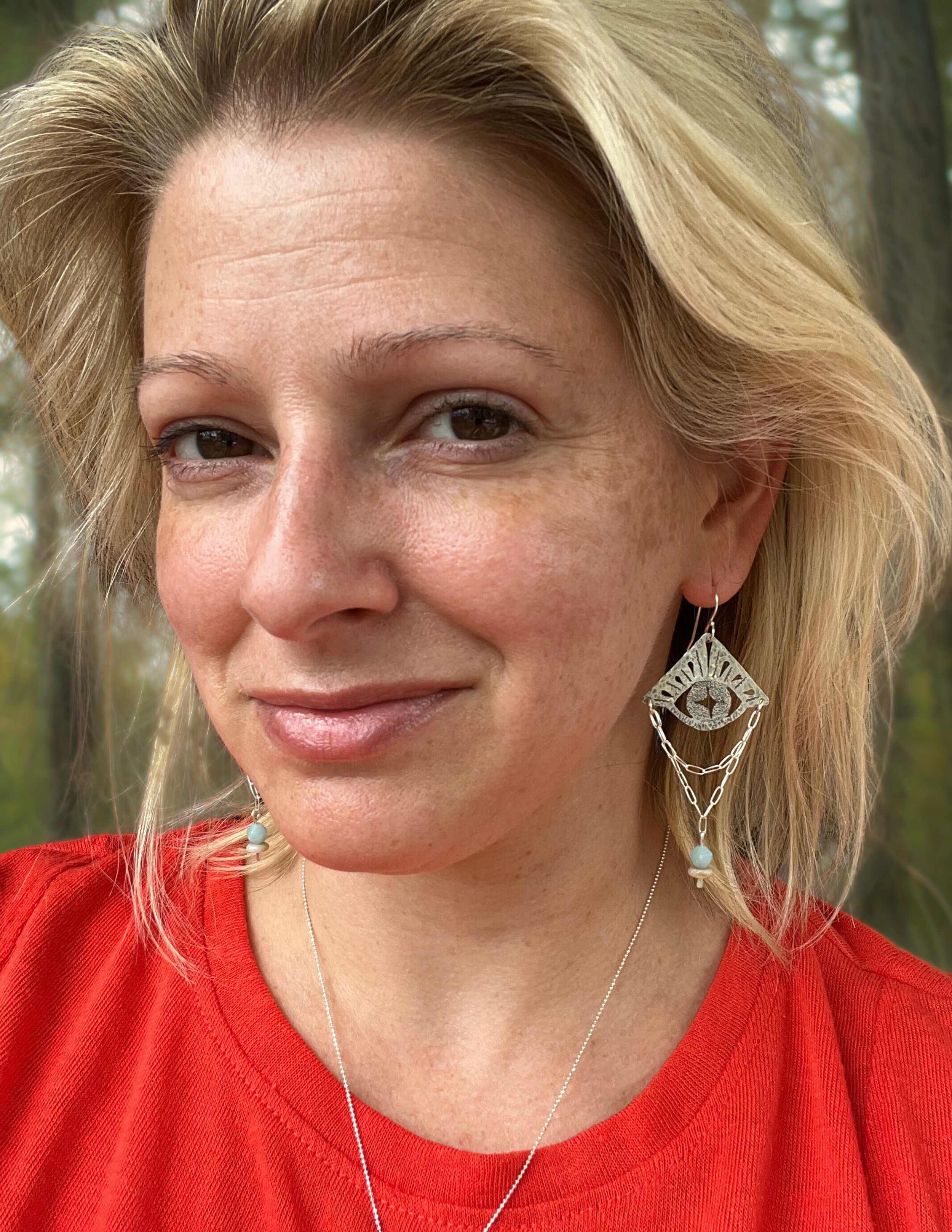Photo of owner and maker Alison Marie wearing a pair of her signature evil eye earrings with amazonite beads.