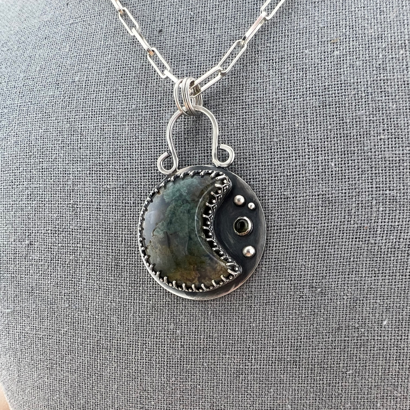 Close-up of moss agate crescent moon pendant showing natural green inclusions and silver detailing.