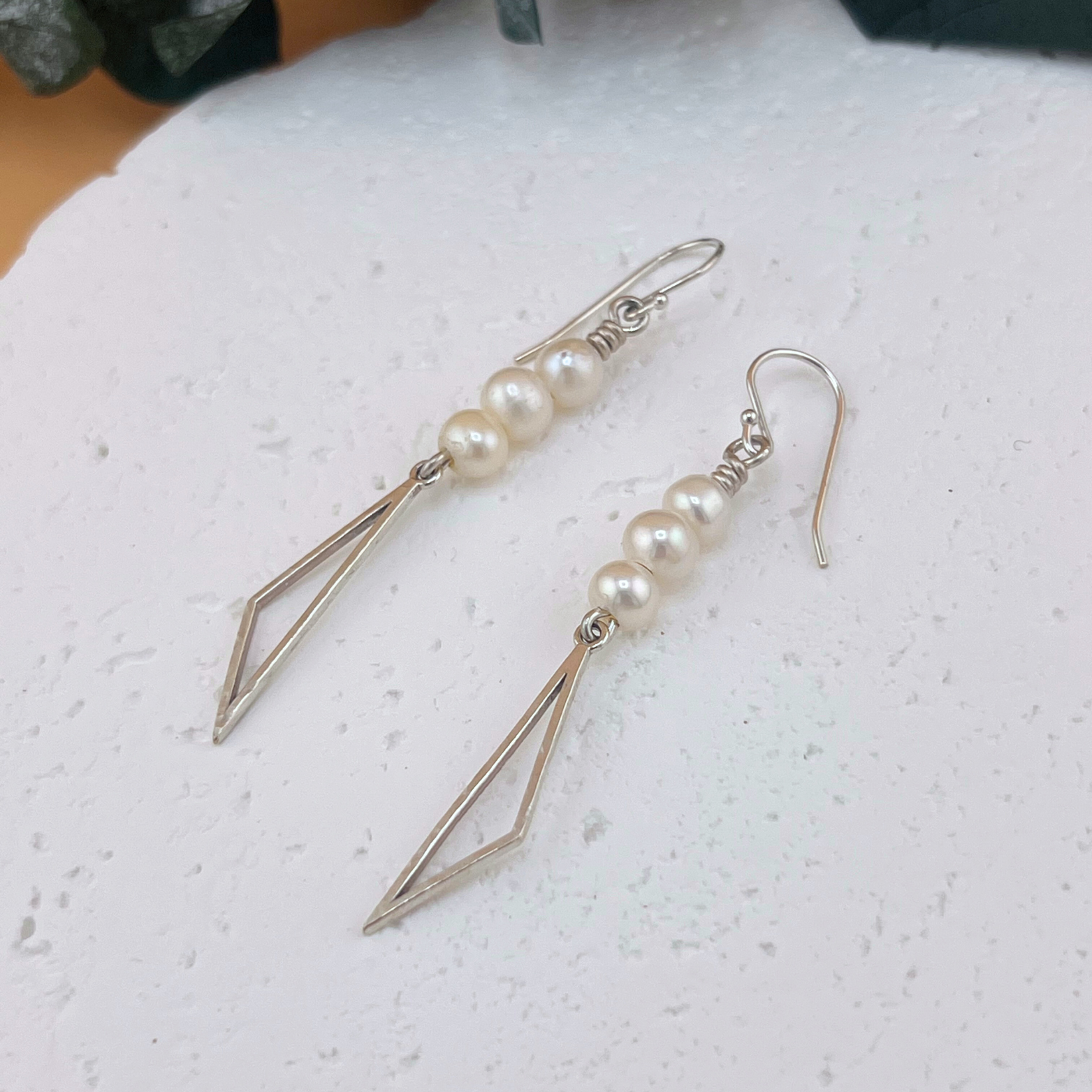 Handmade sterling silver drop earrings with hammered triangular dangles and freshwater pearl accents.