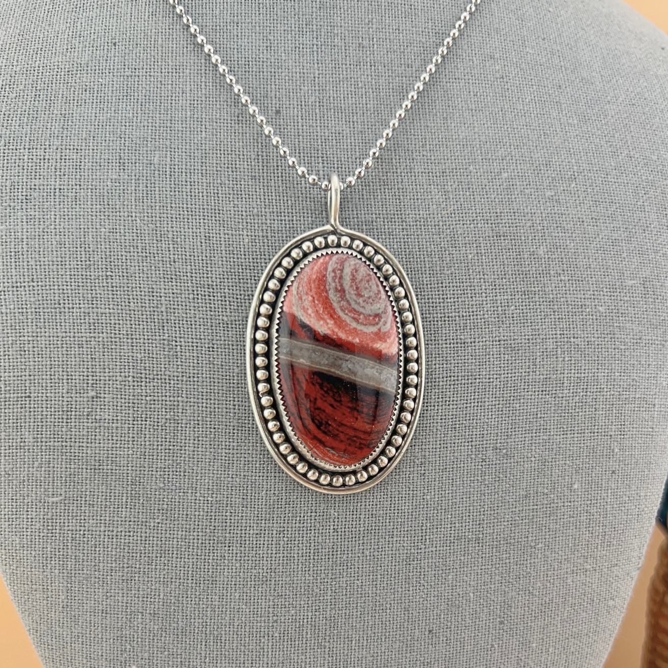 Oval Red River Jasper pendant necklace featuring layered red and earthy tones.