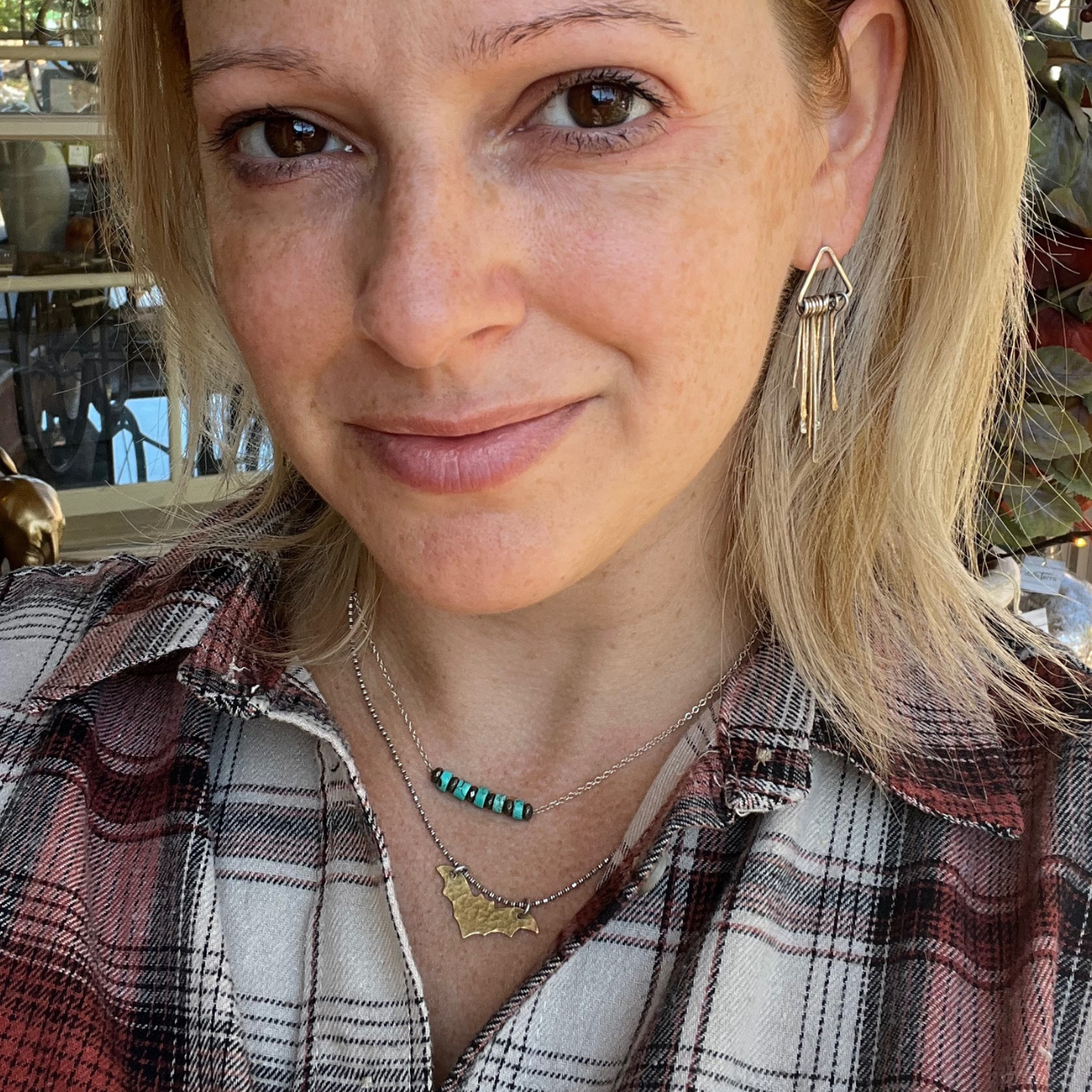 woman wearing the nocturne style brass bat necklace layered with a turquoise and pyrite beaded necklace.