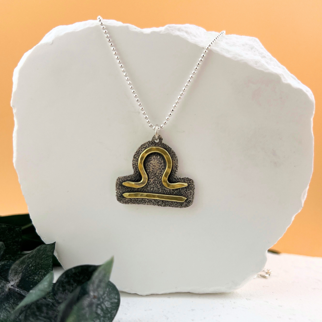 Libra zodiac necklace featuring brass scales symbol on sterling silver.