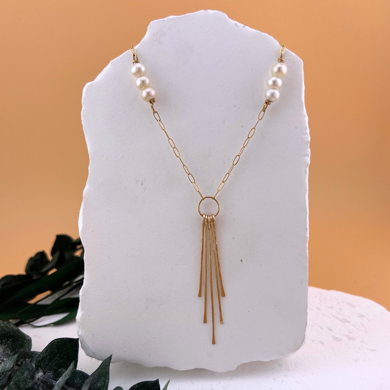 Lumen Fringe Necklace in 14kt gold fill with AAA freshwater pearls and a cascading gold fringe pendant on a minimalist background..