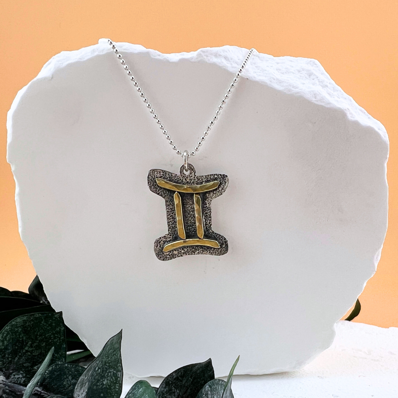 Gemini zodiac necklace with brass twin symbol on sterling silver back plate.