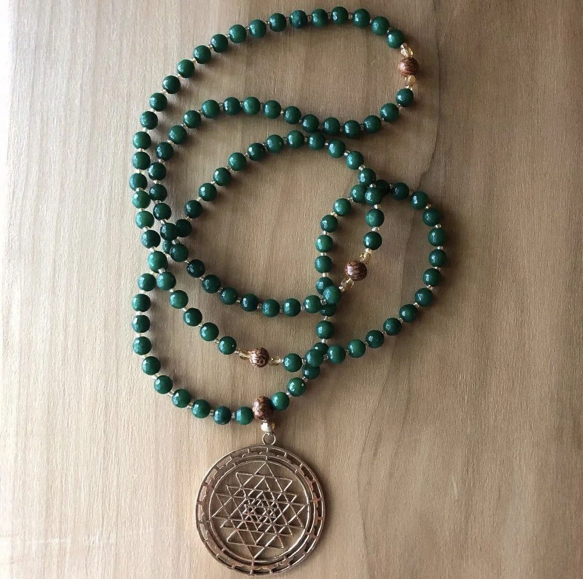 Beaded necklace with green beads, gold accents, and a large gold pendant featuring an intricate geometric pattern.