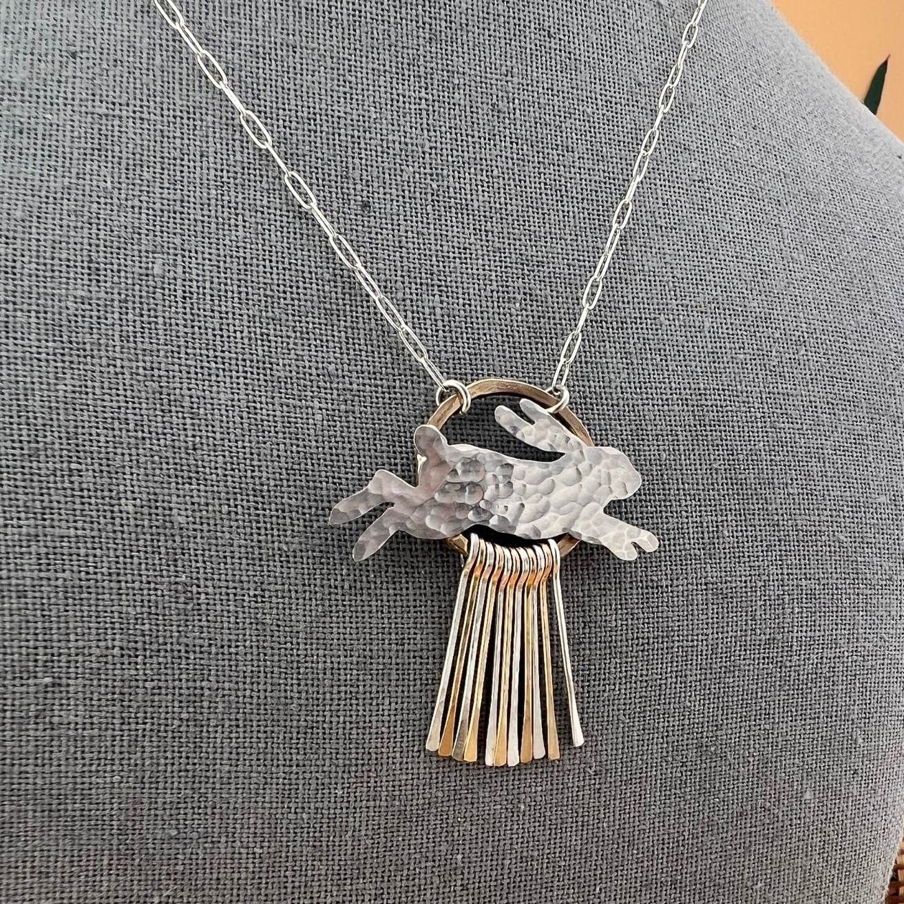 Close-up of sterling silver hare pendant with hammered texture and cascading silver and gold fill fringe accents.