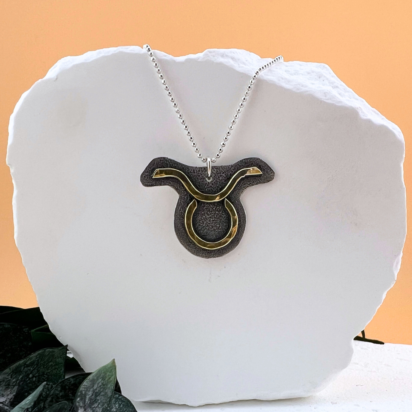 Taurus zodiac necklace featuring brass symbol on textured sterling silver.
