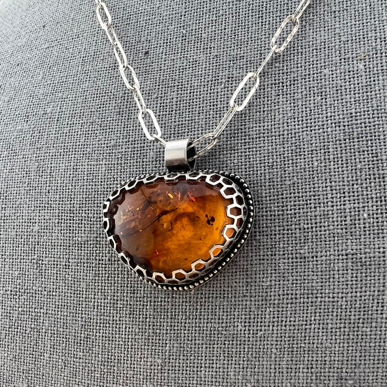 Close-up of honey-toned Baltic amber set in a geometric honeycomb bezel with sterling silver chain.