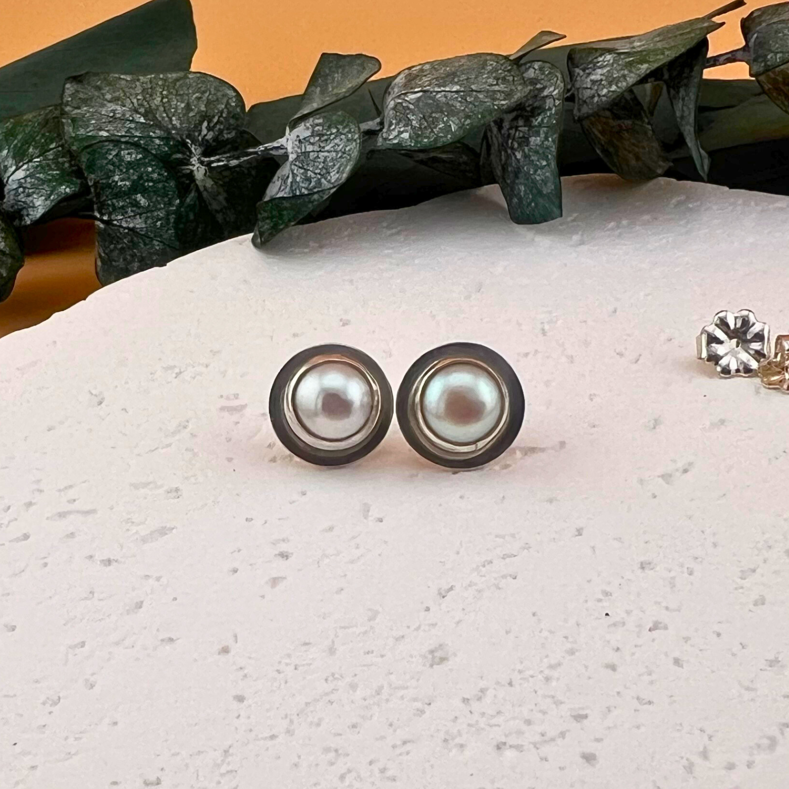 Front facing image of sterling silver pearl stud earrings with a modern handcrafted bezel setting.