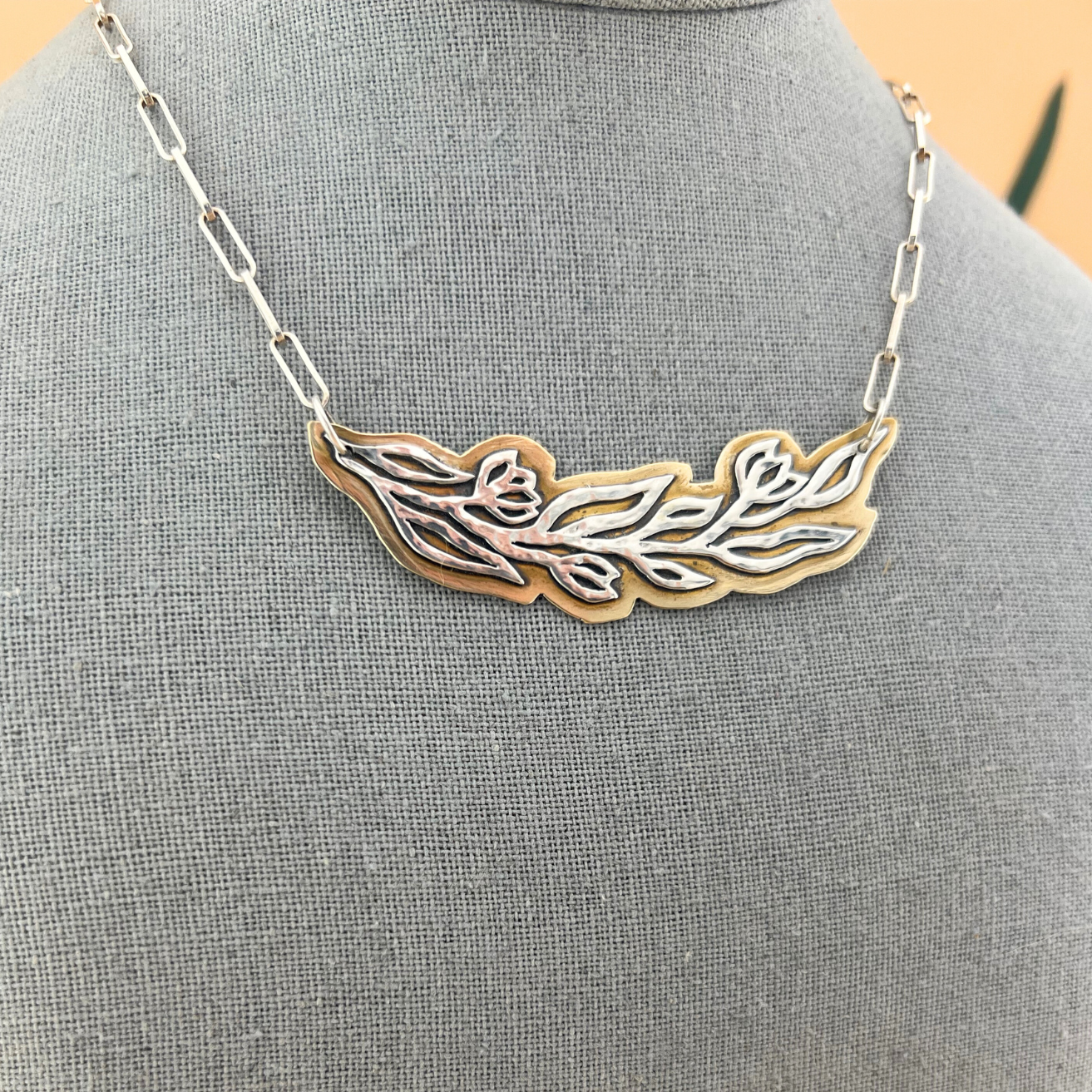 Bold mixed-metal vine statement necklace in sterling silver and brass displayed on a mannequin bust.