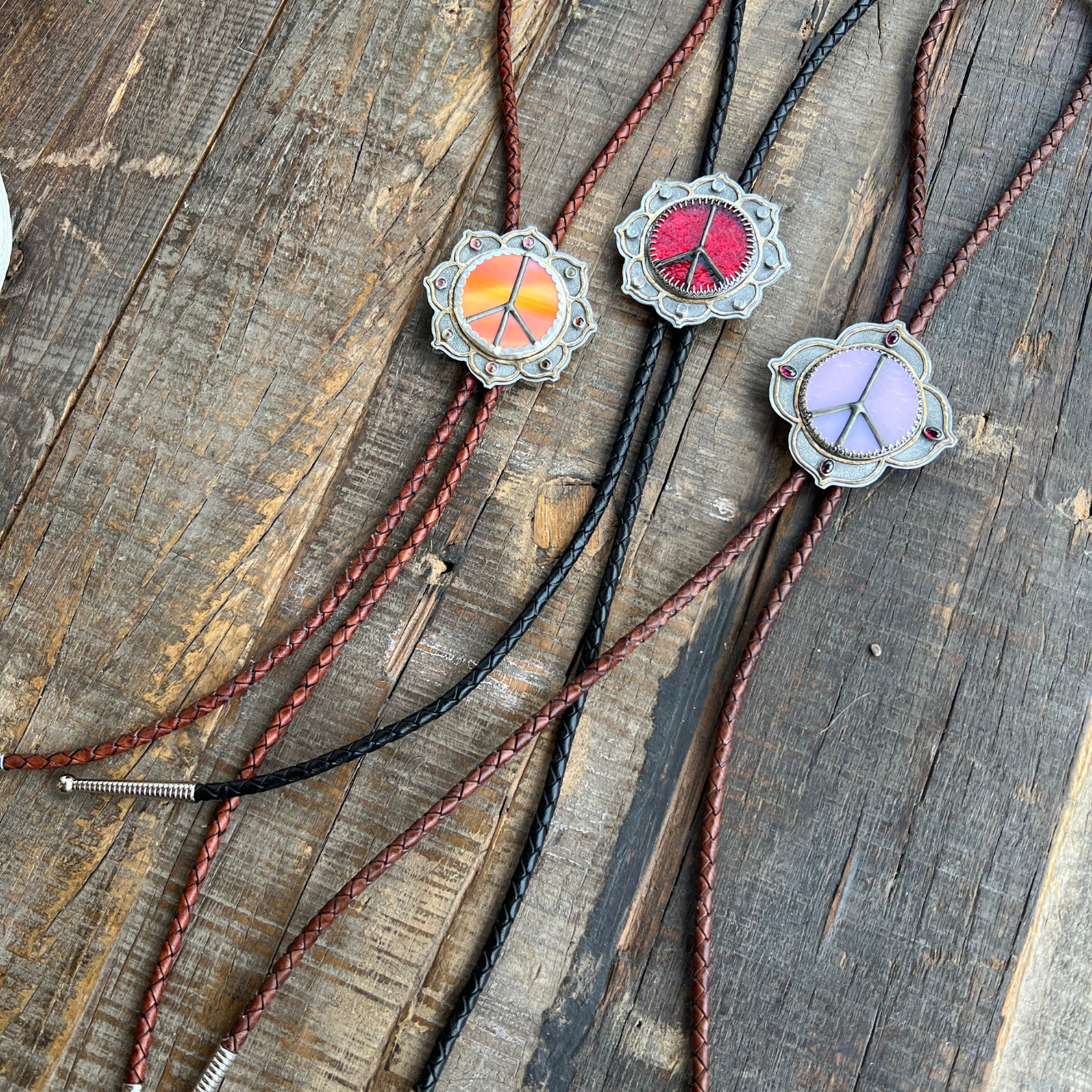 Full-length view of three Peace Portal bolo ties with stained glass centers, brass bolo tips, and gemstone accents displayed together.