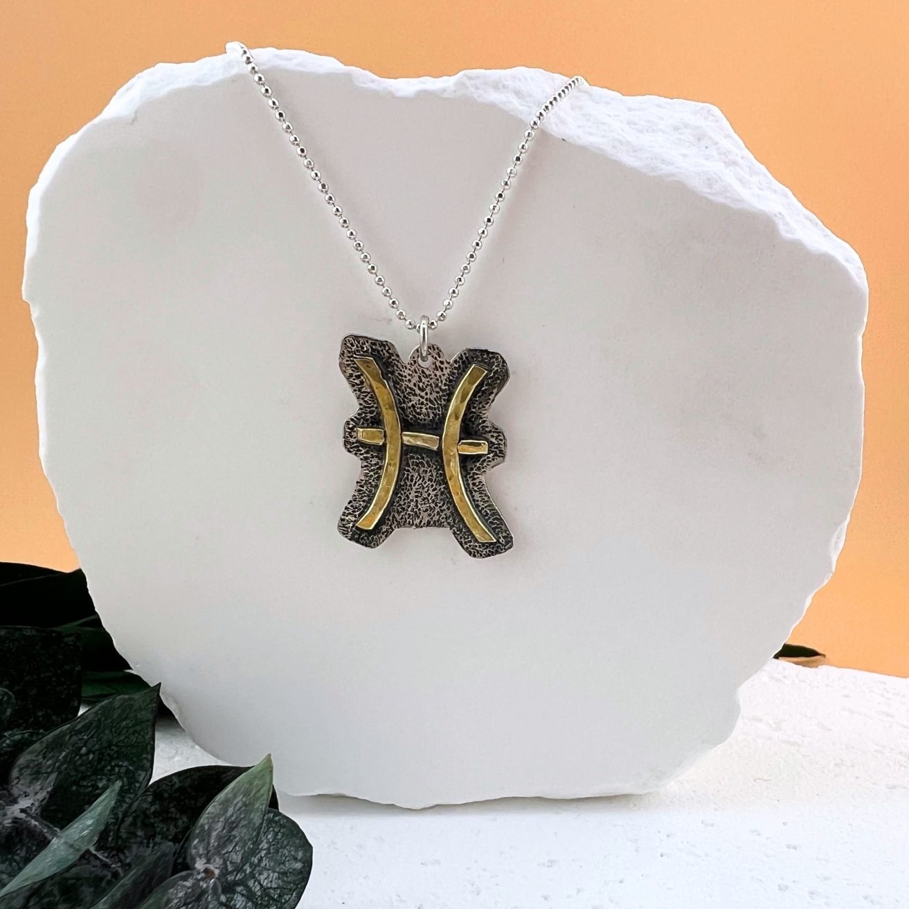 Pisces zodiac necklace with brass fish symbol on textured sterling silver.