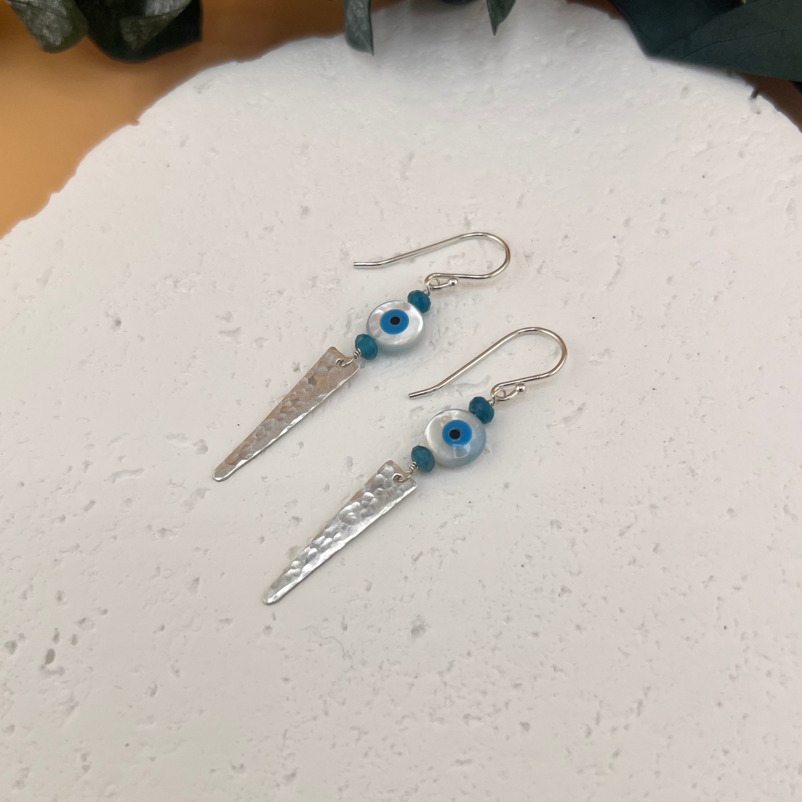 Handmade sterling silver drop earrings with mother-of-pearl evil eye beads, apatite accents, and hammered triangular silver points.