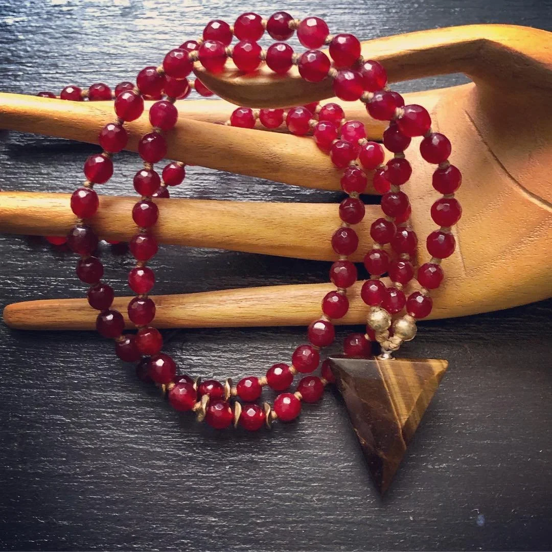 Red beaded necklace with a triangular pendant, placed on a wooden display with a dark background.