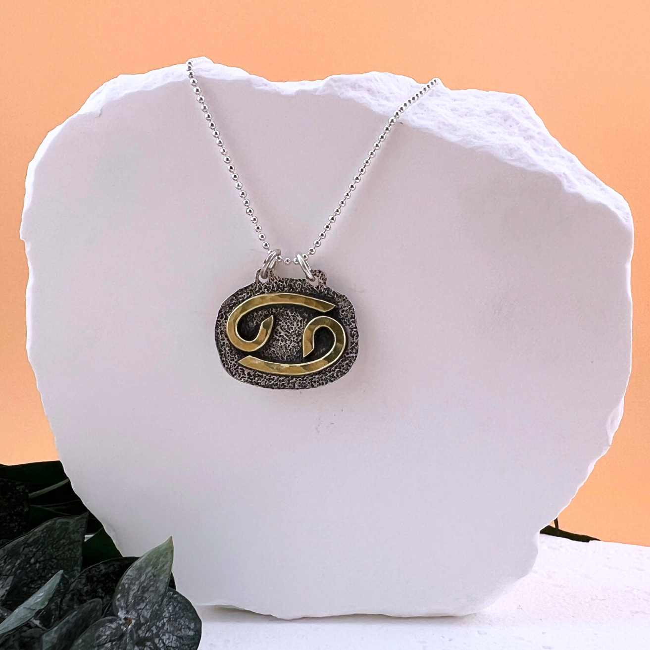 Cancer zodiac necklace with brass crab symbol on textured sterling silver.