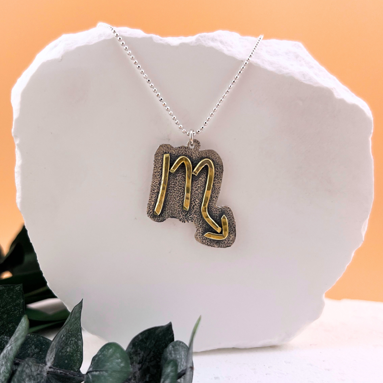 Scorpio zodiac necklace with brass symbol on textured sterling silver pendant.